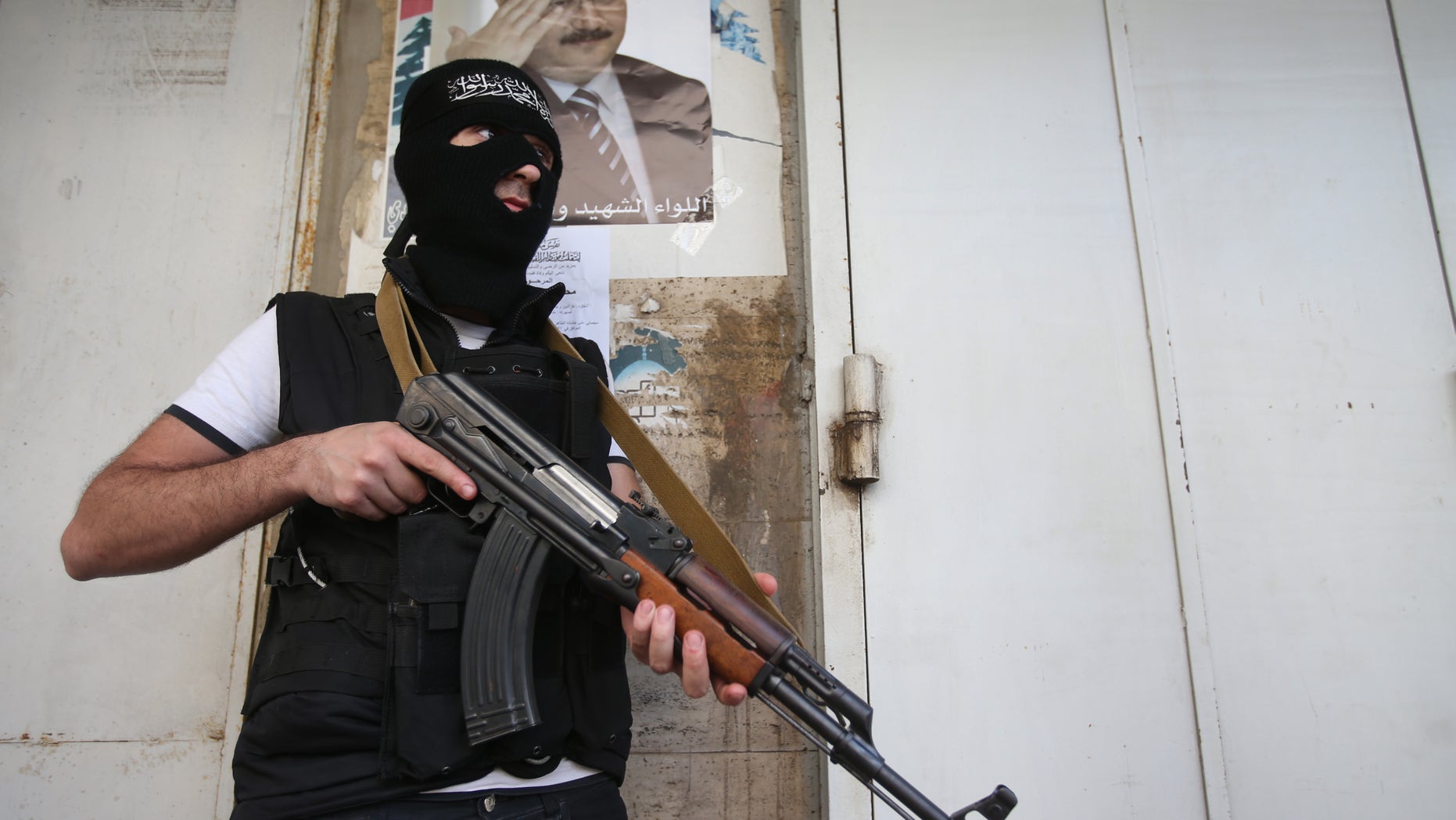 A masked Sunni gunman stands guard under a portrait of Brig. Gen. Wissam al-Hassan, who was assassinated on Friday by a car bomb, on a blocked street leading to a Shiite neighborhood after overnight clashes that erupted between Sunni and Shiite gunmen in Beirut, Lebanon, Monday Oct. 22, 2012. Lebanese security officials say overnight clashes in Beirut between Sunni and Shiite gunmen have wounded several people. The officials say troops managed to separate the gunmen and calm returned Monday morning to the two neighborhoods in the capital where fighting had erupted. (AP Photo/Hussein Malla)