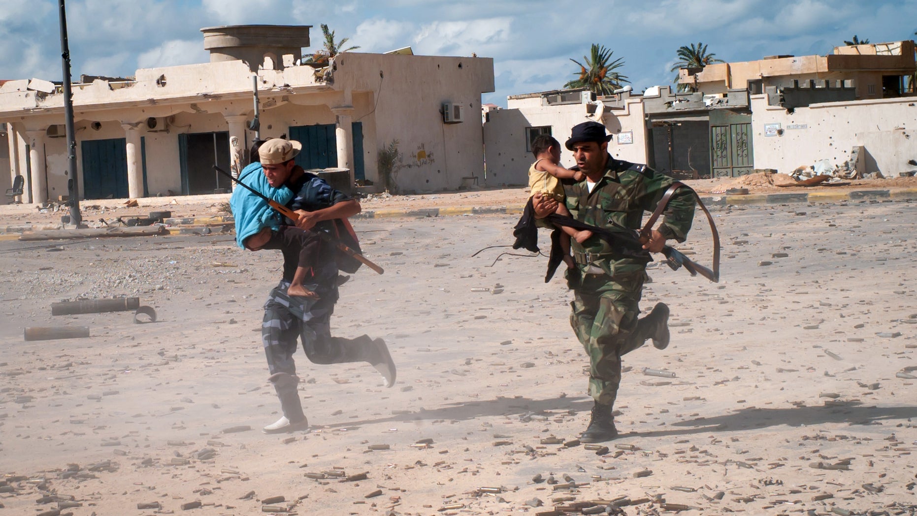 Oct. 17, 2011: Revolutionary fighters run across the street under heavy sniper fire carrying Bangladeshi children who were trapped in Sirte, Libya, during the entire siege of the city.