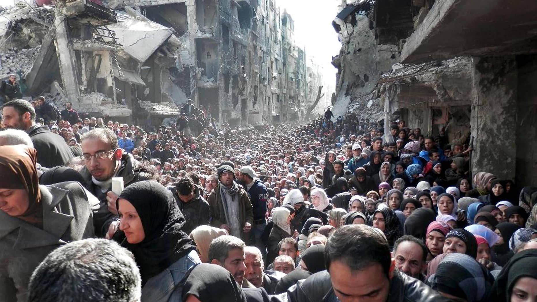 FILE - In this Jan. 31, 2014, file photo, released by the United Nations Relief and Works Agency for Palestine Refugees in the Near East (UNRWA), shows residents of the besieged Palestinian camp of Yarmouk, queuing to receive food supplies, in Damascus, Syria. UNRWA spokesman Christopher Gunness says the agency needs around $250 million to fund its cash program, which provides cash distributions for roughly half a million Palestinian refugees affected by the war in Syria. (AP Photo/UNRWA, File)
