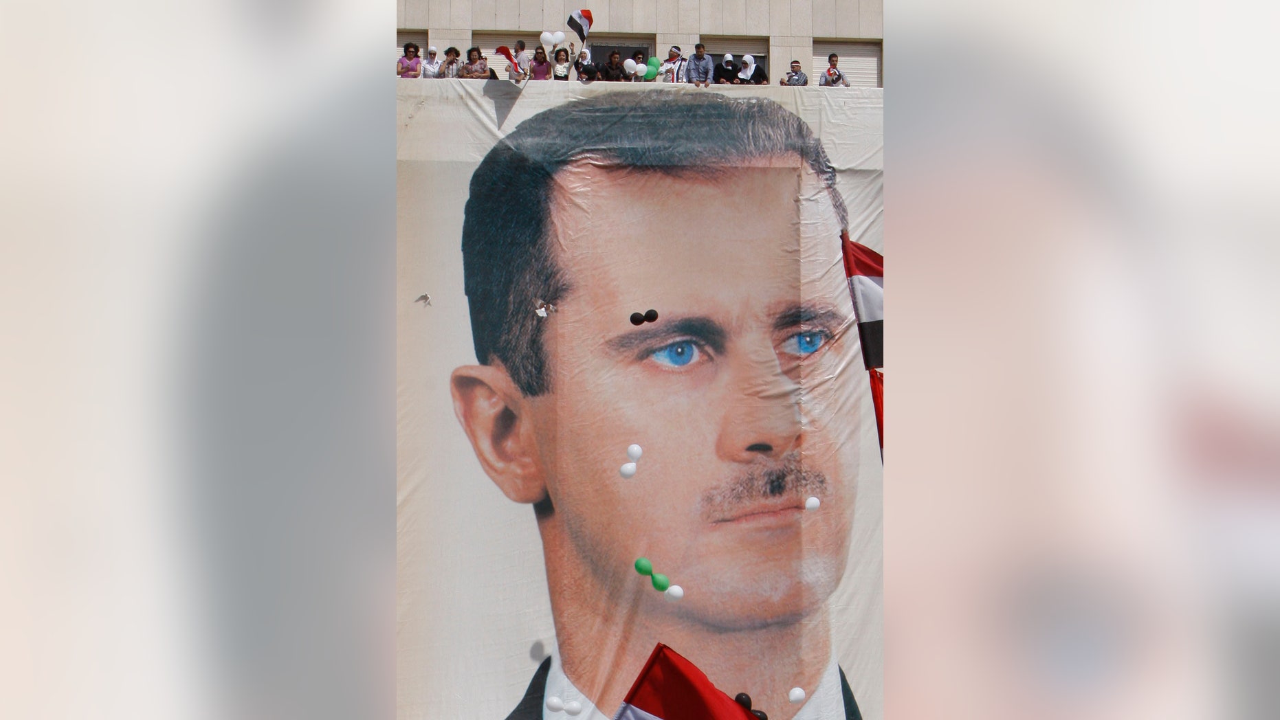 Syrian regime supporters stand on a roof as balloons float near a huge portrait of Syian President Bashar Assad during a demonstration to show their support for their President and to thank Russia and China for blocking a U.N. Security Council resolution condemning Syria for its brutal crackdown, in Damascus, Syria, on Wednesday Oct. 12, 2011.
