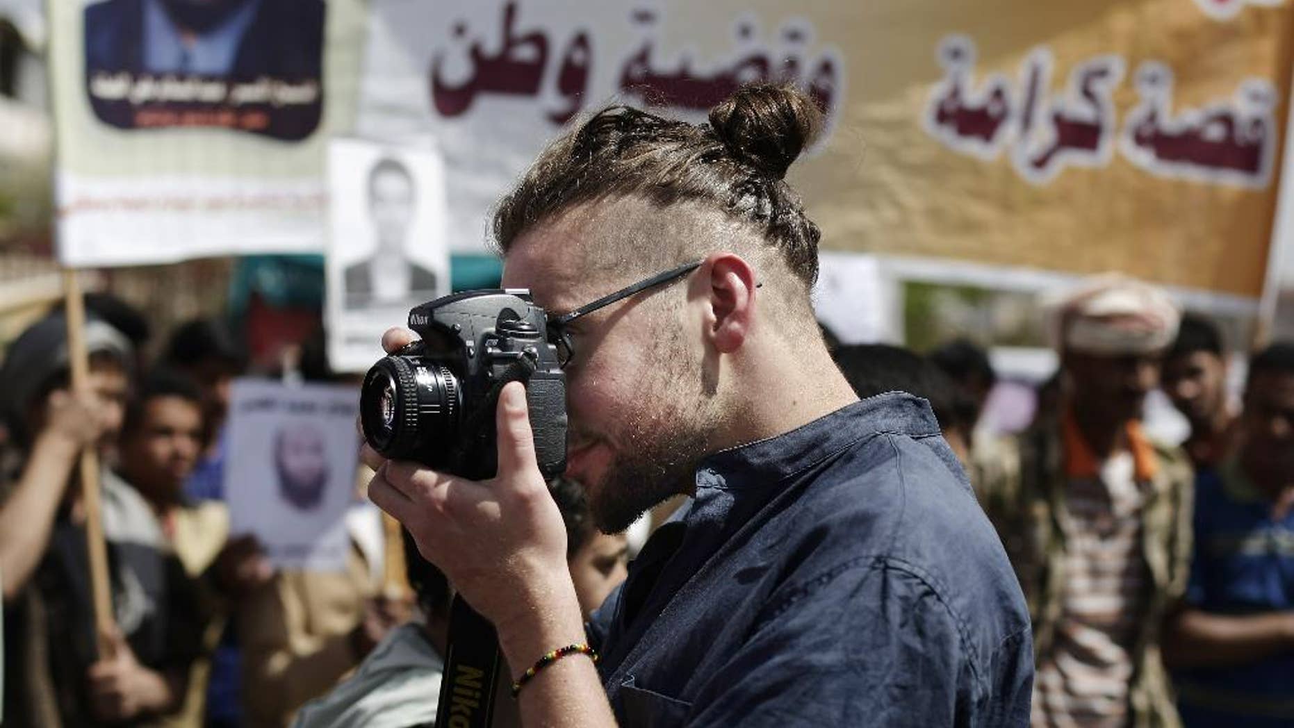 In this Tuesday, April 16, 2013 photo, Luke Somers, 33, an American photojournalist who was kidnapped over a year ago by al-Qaida, uses a camera during a demonstration demanding the release of Yemeni detainees in Guantanamo Bay prison in front of the U.S. embassy in Sanaa, Yemen. Somers and a South African teacher held by al-Qaida militants in Yemen were killed Saturday, Dec. 6, 2014 during a U.S.-led rescue attempt, a raid President Barack Obama said he ordered over an "imminent danger" to the reporter. (AP Photo/Hani Mohammed)
