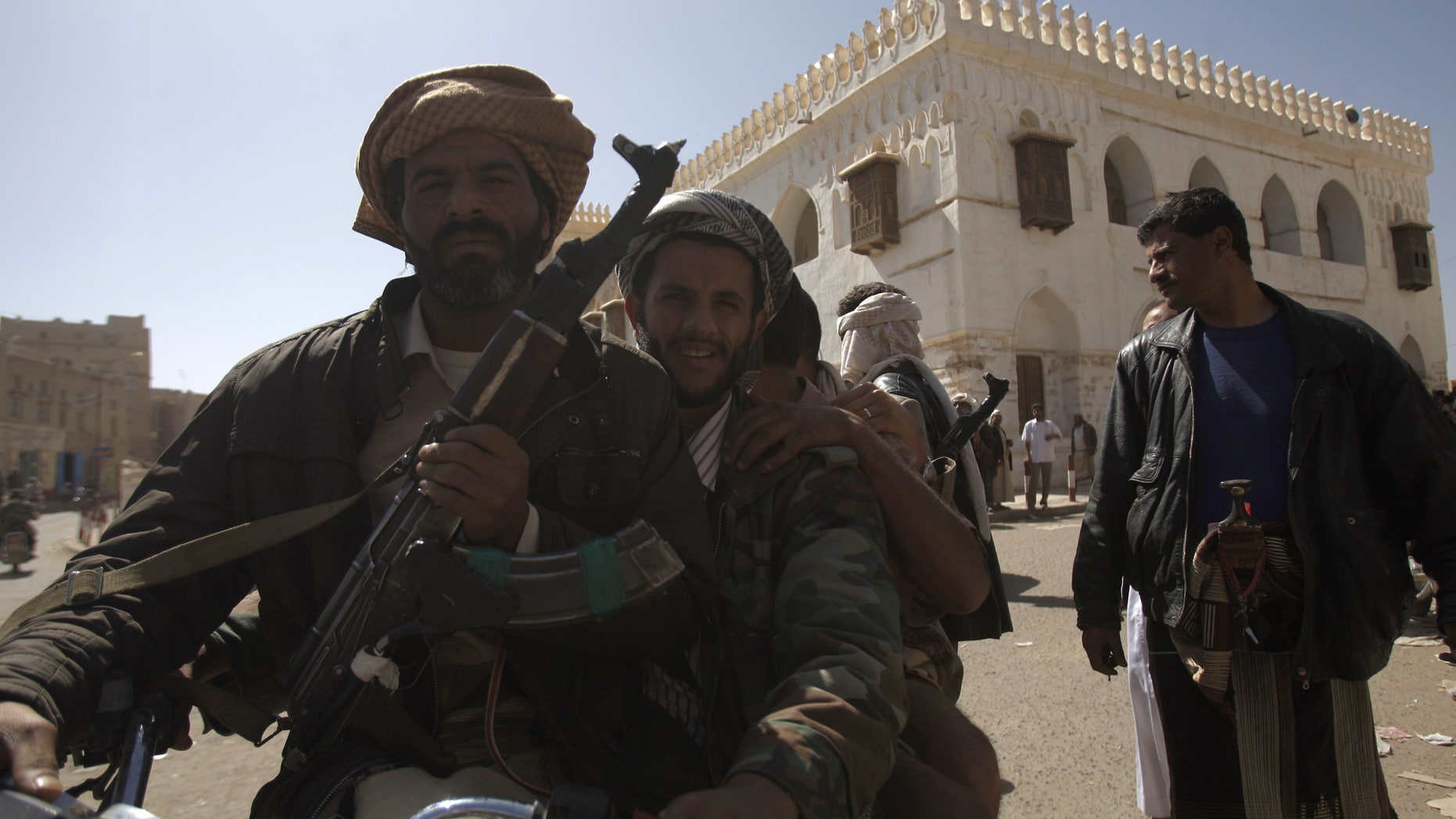 Jan. 25, 2012: Backdropped by Ameriyah religious school which was seized by Al Qaeda militants, a Yemeni armed tribesman, left, holds his rifle as he rides a motorcycle with others in Radda town, 100 miles south of the capital Sanaa, Yemen.