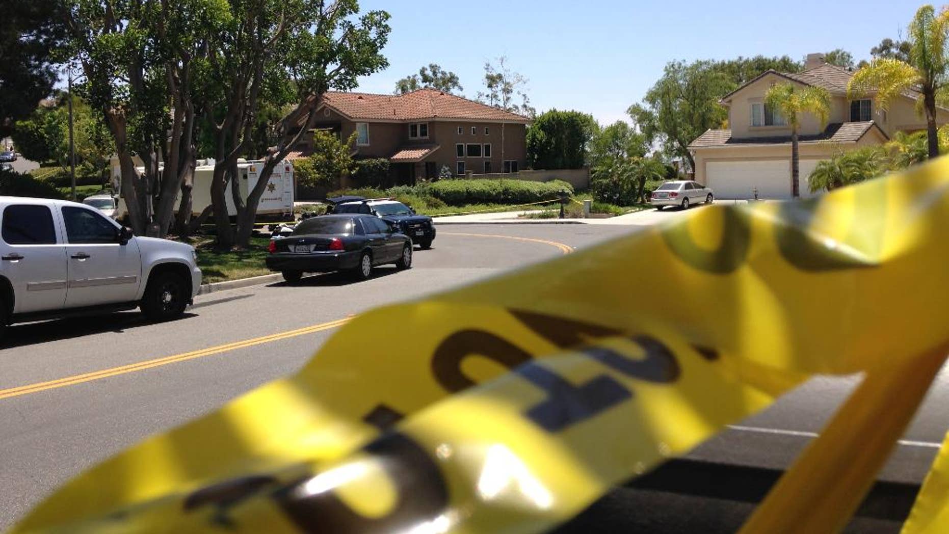 Police tape closes a street where four people were found dead in a home, center, on Tuesday, May 27, 2014 in suburban Mission Viejo, Calif. Authorities said the bodies were found by Orange County deputies making a welfare check after a relative's emergency call. The dead people were only described as two males and two females, and the Sheriff's Department was not releasing any information on how they may be related.(AP Photo/Gillian Flaccus)