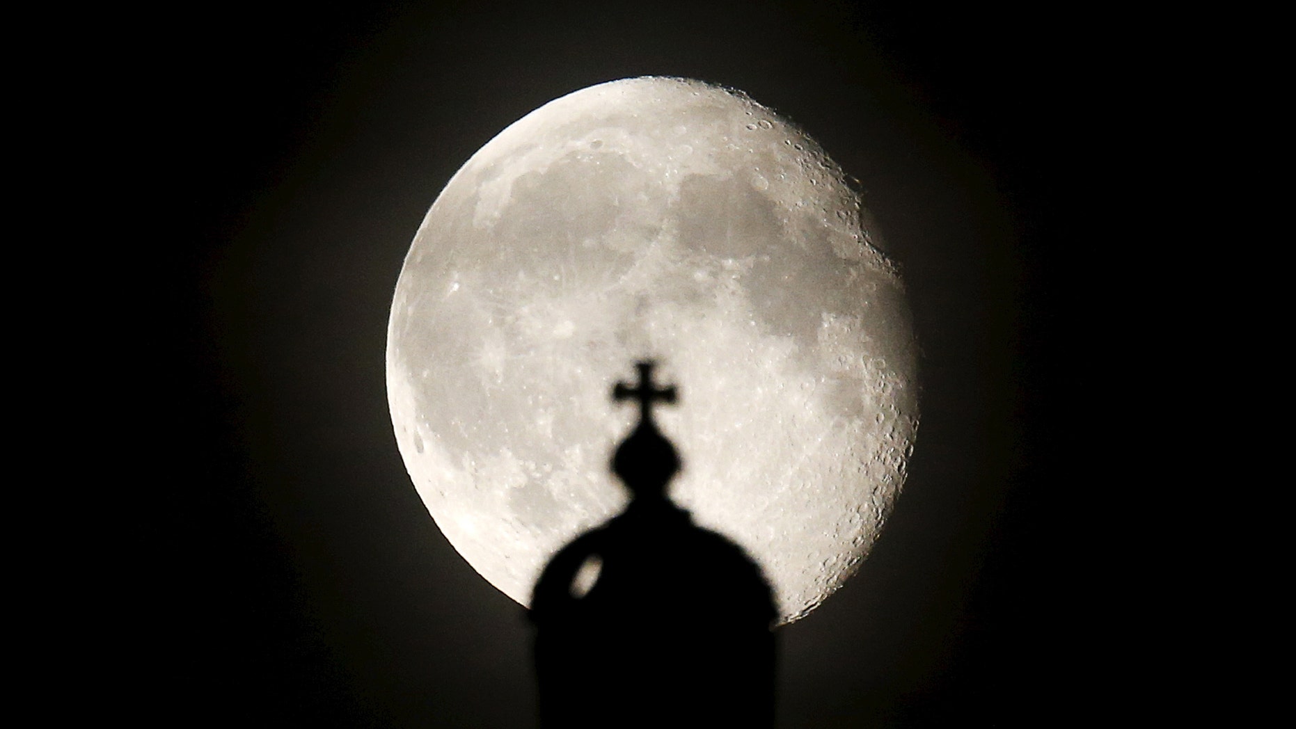 The moon rises next to a cross atop of the Reichstag building in Berlin, Germany, Aug. 2, 2015.