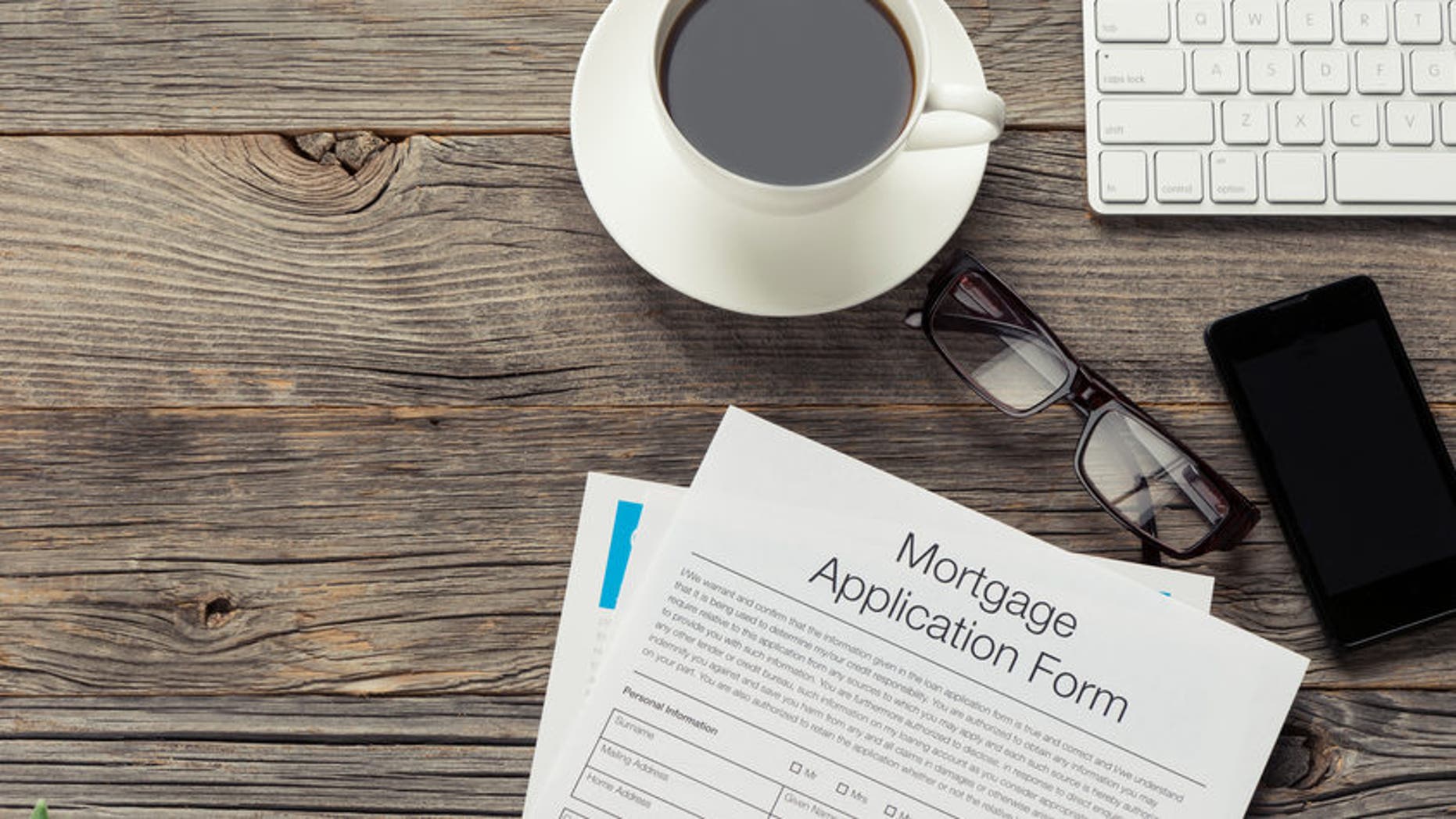 Mortgage application form on wooden table. There is also a mobile phone, computer keyboard, coffee, Filofax organizer notepad and glasses on the table. The table is made of wood and is quite old. Copy space on left.