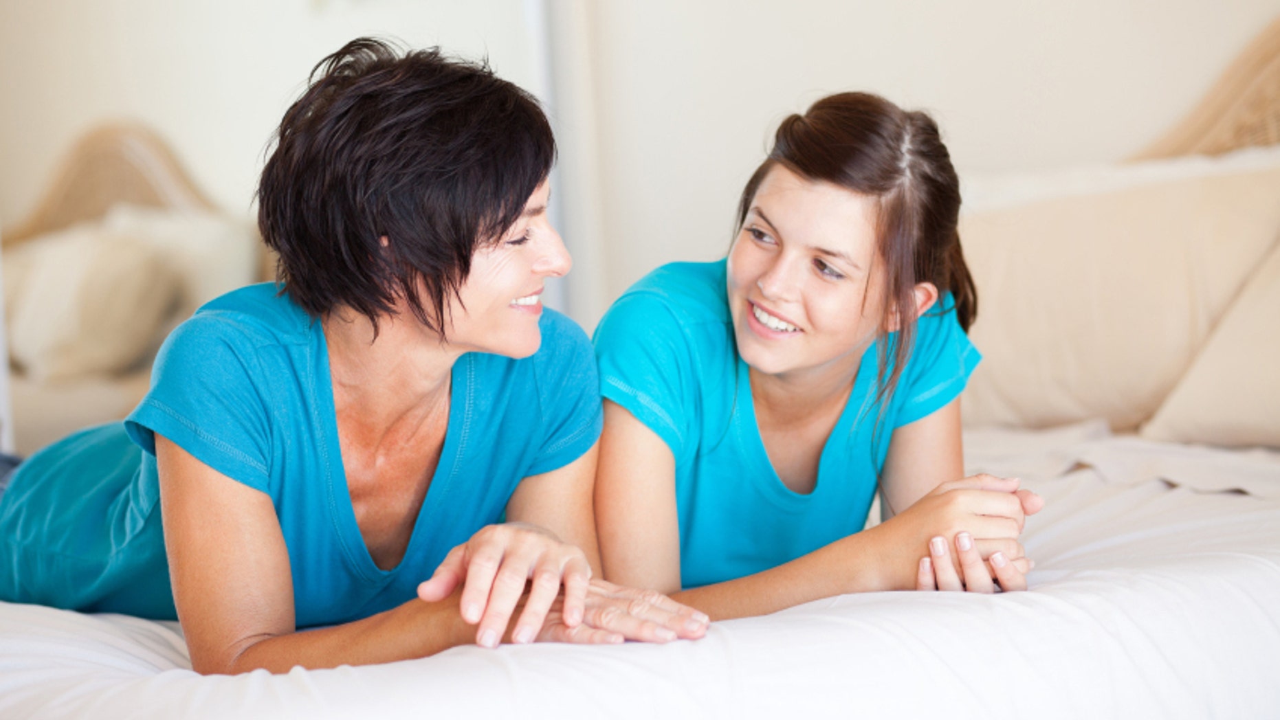 middle aged mother and teen daughter chatting on bed