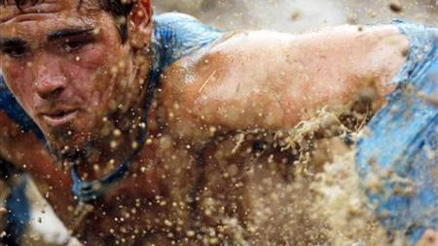 July 15, 2012: Mud flies in front of a competitor as he swims through mud underneath electrified wires during the Tough Mudder at Mt. Snow in West Dover, Vermont.