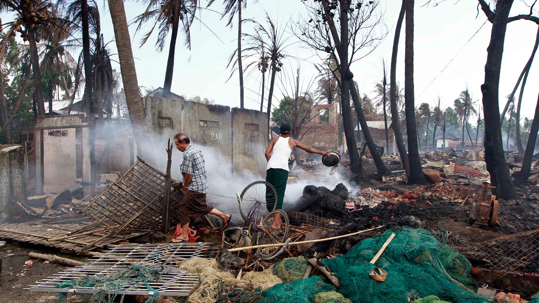 June 11, 2012: A man pours water on the debris of a burned house still smoldering as another man walks by in Sittwe, Myanmar.