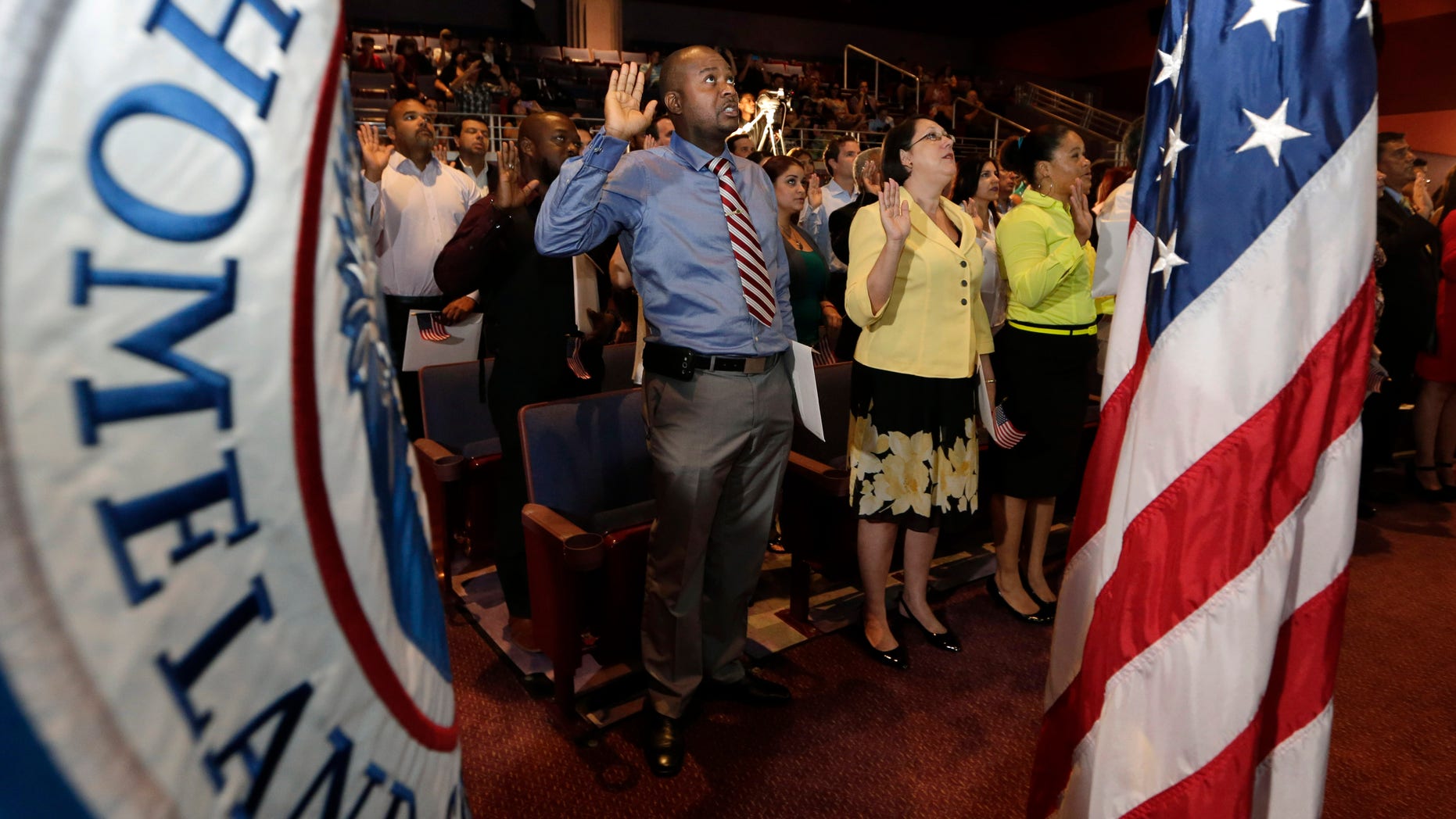 Jean Naason, 39, of Haiti, left, recites the "Oath of Allegiance" during a naturalization ceremony administered by the U.S. Citizenship and Immigration Services (USCIS), Thursday, June 5, 2014, in Miami. Fifty candidates from various countries became U.S. citizens in celebration of the launch of the first annual Immigrant Heritage Month. (AP Photo/Lynne Sladky)