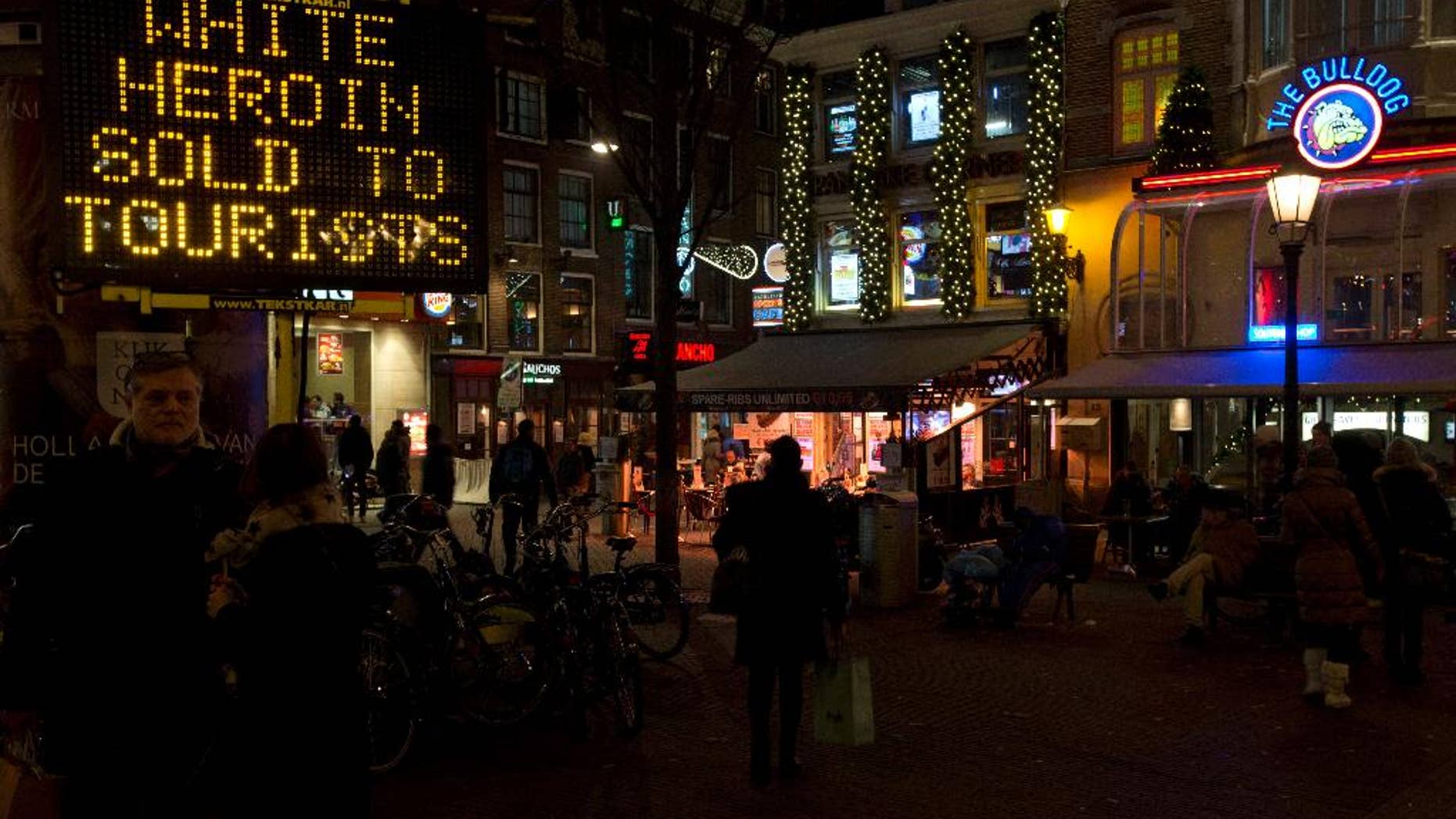 FILE - In this Dec. 5, 2014 file photo an electronic sign outside Amsterdam's famous Bulldog coffee shop, right, warns tourists of "white heroin", an extremely dangerous drug which is being sold as cocaine to tourists in Amsterdam. Police in Amsterdam said Tuesday April 7, 2015, that a 42-year-old man who turned himself in on Saturday could be a dealer who sold white heroin to tourists, telling them that it was cocaine, three tourists have died in recent months and 20 other became unwell after taking heroin. (AP Photo/Peter Dejong, File)