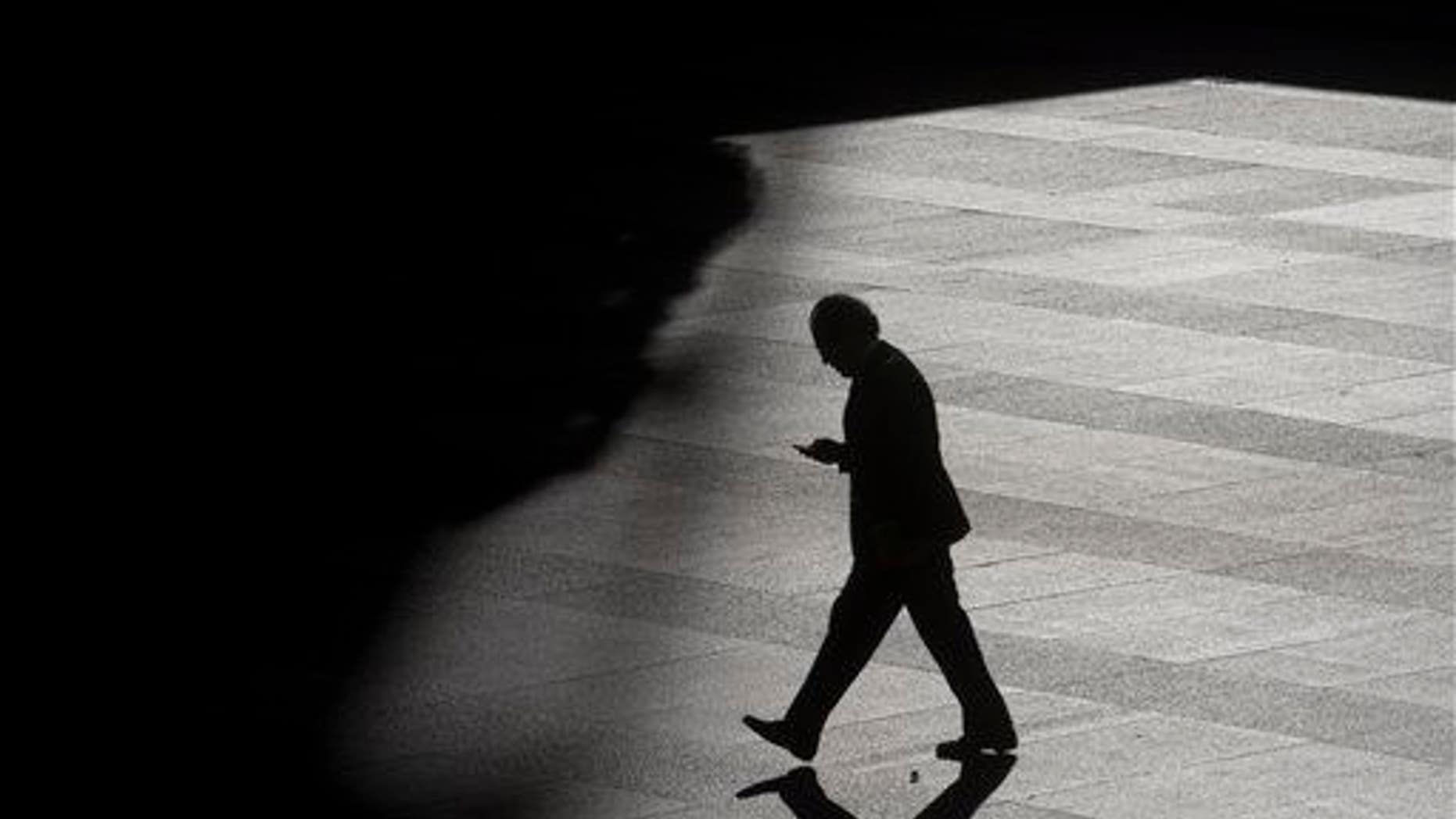 A man looks as his cell phone as he walks into the shadows.