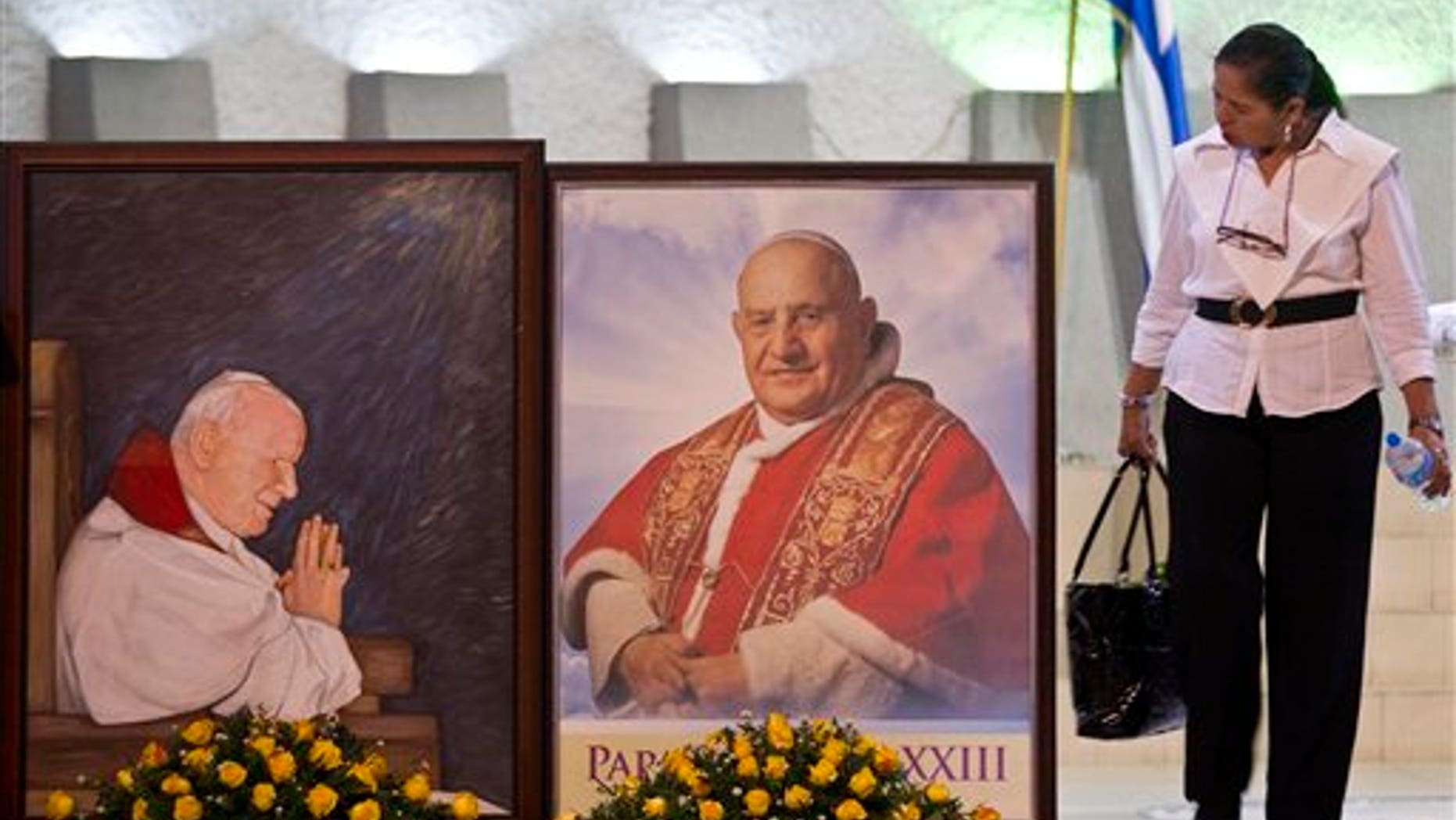 A woman walks next to portraits of late Pope John Paul II, left, and Pope John XXIII before a vigil at a Metropolitan cathedral in Managua, Nicaragua, Saturday, April 26, 2014. The banner reads in Spanish "We celebrate the lives of two men who fought to make this a better world." About 1 million pilgrims are expected to be witnesses in Rome as retired pontiff Benedict XVI will help Pope Francis celebrate the sainthood ceremony Sunday for John Paul II and John XXIII, setting the stage for an unprecedented occurrence of two living popes canonizing two of their predecessors. (AP Photo/Esteban Felix)
