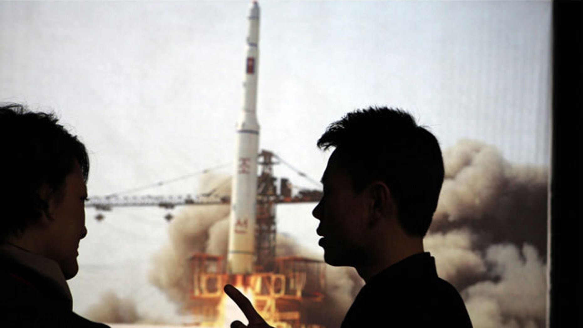 In this photo taken Tuesday, April 10, 2012, North Korean guide Kim Won Ho, right, speaks to a foreign journalist near a photo depicting the 2009 satellite rocket launch at the Three Revolutions exhibition hall in Pyongyang, North Korea.
