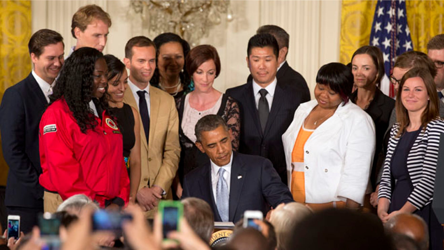 Surrounded by college students, President Barack Obama signs a Presidential Memorandum on reducing the burden of student loan debt, Monday, June 9, 2014, in the East Room of the White House in Washington.