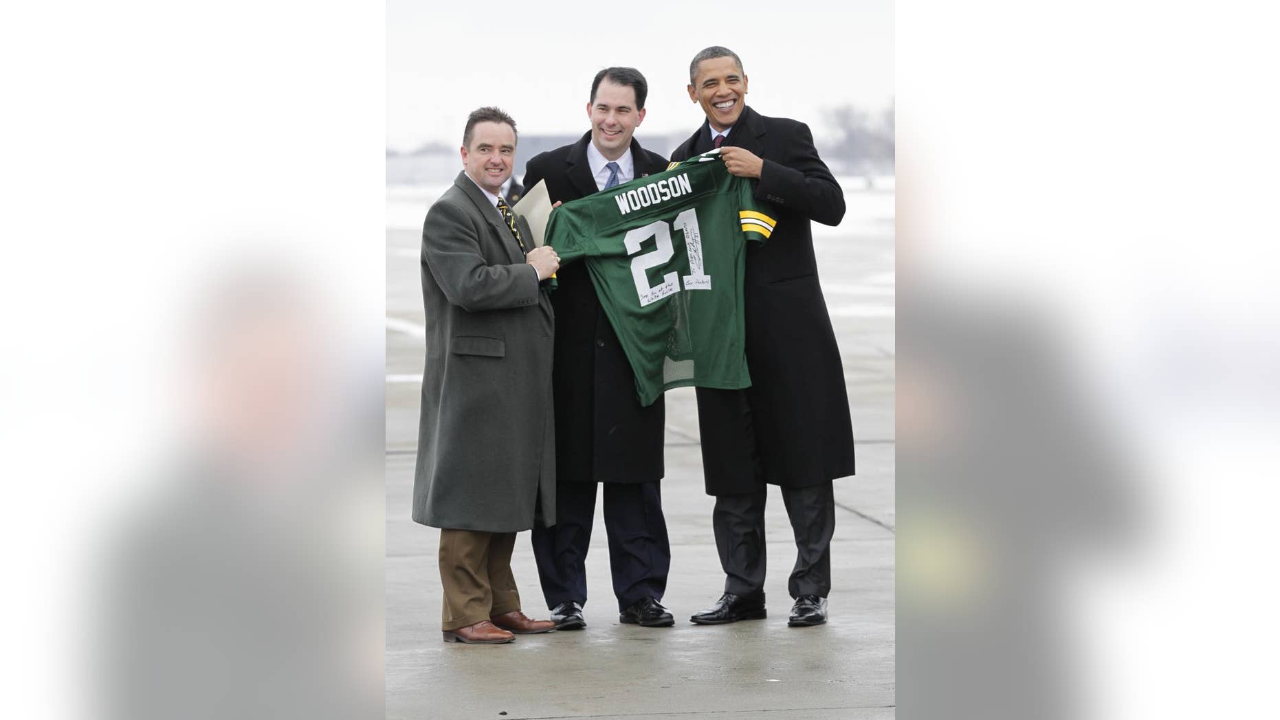 President Barack Obama receives an autographed Green Bay Packers Charles Woodson from Wisconsin Gov. Scott Walker, center, and Green Bay Mayor Jim Schmitt, upon his arrival in Green Bay, Wis., Wednesday, Jan. 26, 2011, en route to nearby Manitowoc, Wis., where he will a tour renewable-energy factories and talk about jobs and the economy. Obama, a Chicago native, predicted the Chicago Bears would beat Green Bay in the NFC Championship game. (AP Photo/J. Scott Applewhite)