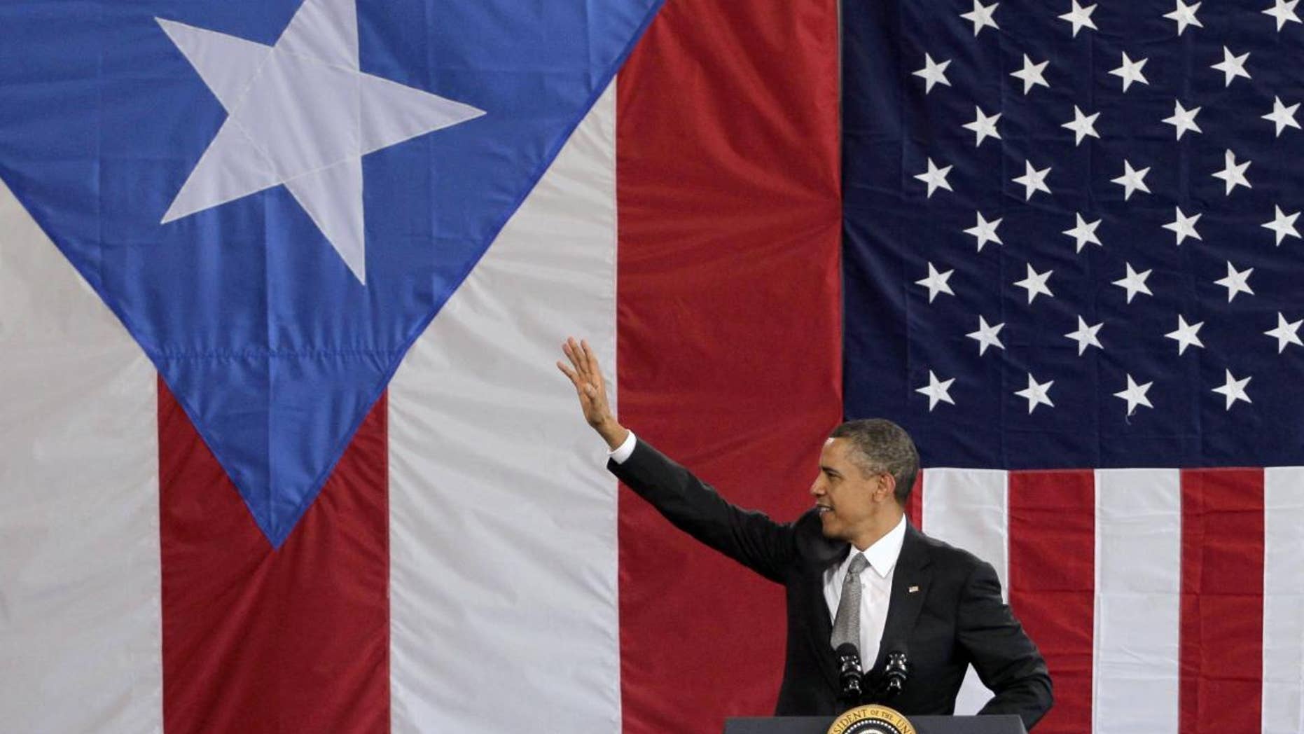 President Barack Obama waves to a crowd gathered inside a hangar at the Muniz Air National Guard Base, shortly after his arrival in San Juan, Puerto Rico, Tuesday, June 14, 2011. Obama's visit to Puerto Rico marks the first by a sitting U.S. President since John Kennedy. Obama is backed by Puerto Rican and American flags. (AP Photo/Brennan Linsley)
