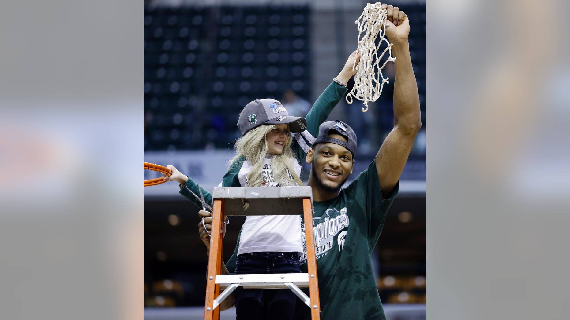 FILE - In this March 16, 2014 file photo, Michigan State forward Adreian Payne, right, hoists the net with Lacey Holsworth, who is battling cancer, after Michigan State defeated Michigan 69-55 in an NCAA college basketball game in the championship of the Big Ten Conference tournament in Indianapolis. The father of 8-year-old Lacey Holsworth, who befriended Michigan State basketball star Adreian Payne says his daughter has died. Matt Holsworth says Lacey Holsworth died at their St. Johns, Mich., home late Tuesday, April 8, 2014 "with her mommy and daddy holding her in their arms." (AP Photo/Michael Conroy, File)