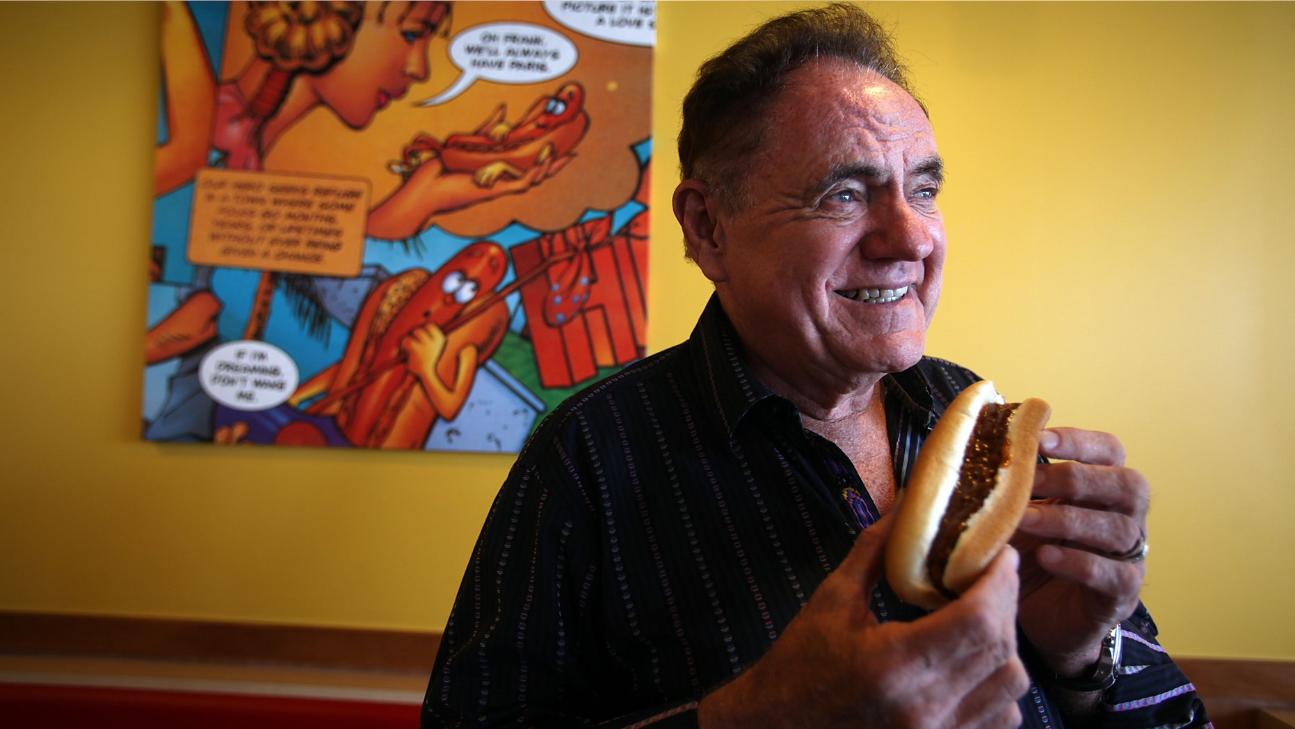 John Galardi, founder of the hot dog chain Wienerschnitzel, poses for a portrait in Lakewood, Calif. He is holding a chili dog.