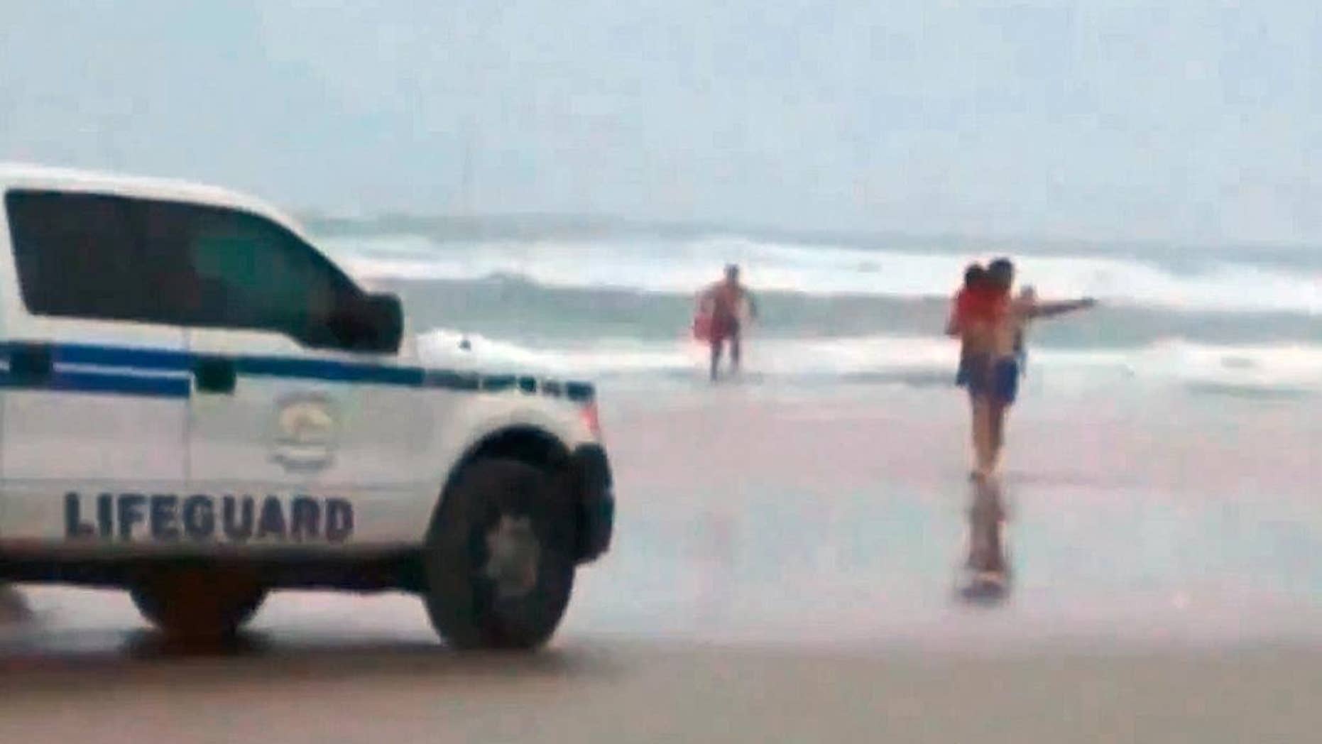 In this image made from video and released by Simon Besner, lifeguards rescue children from a minivan that their mother drove into the Atlantic, Tuesday, March 4, 2014 in Daytona Beach, Fla. Ebony Wilkerson, 31, a pregnant South Carolina woman who drove a minivan carrying her three young children into the ocean surf off Florida had talked about demons before leaving the house, according to her sister who worriedly called police, officials said during a news conference Wednesday. Bystanders and officers helped pull Wilkerson and her children, ages 3, 9 and 10, from their minivan. The children were turned over to welfare authorities. The Volusia County Sheriff's Office says Wilkerson was undergoing a mental evaluation. (AP Photo/Simon Besner)