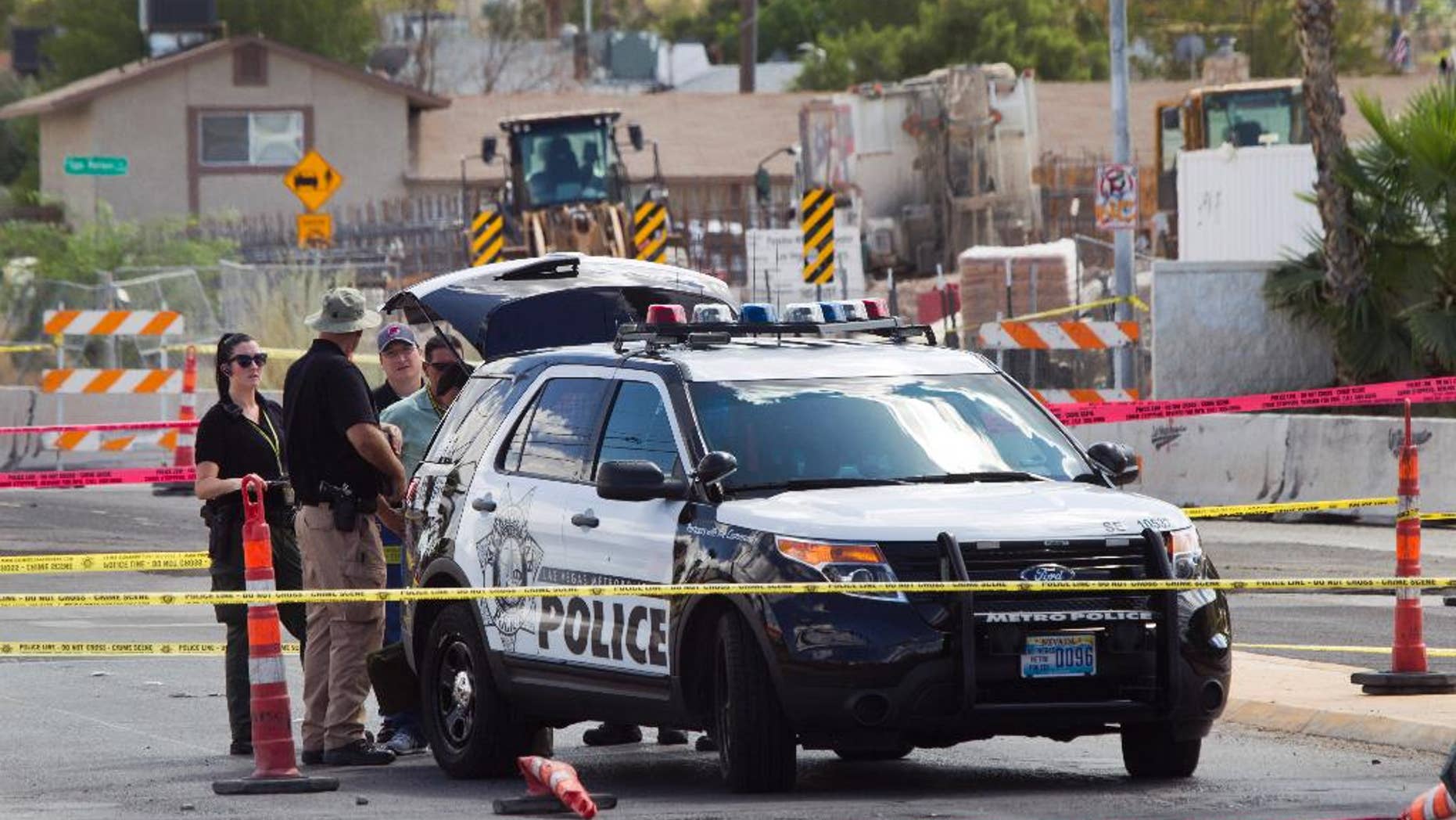 In this Sept. 6, 2015, photo, investigators stand by a Las Vegas Metro Police patrol vehicle after an officer in the vehicle was shot in Las Vegas. A man with a handgun walked up to the SUV as it was waiting at a red light and opened fire, striking one officer in the hand, authorities said. (Steve Marcus/Las Vegas Sun via AP) LAS VEGAS REVIEW-JOURNAL OUT; MANDATORY CREDIT