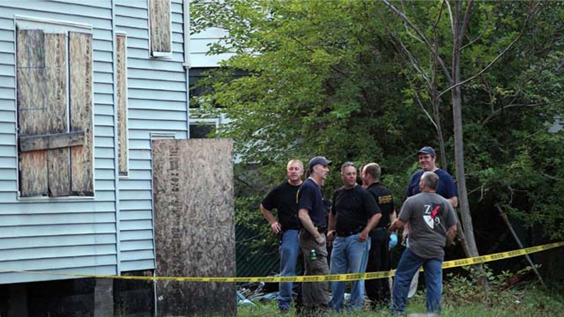 July 20, 2013: Law enforcement and FBI stand at the back of a boarded-up home where bodies were found earlier in the day Saturday in East Cleveland, Ohio. (AP Photo/The Plain Dealer, Joshua Gunter)