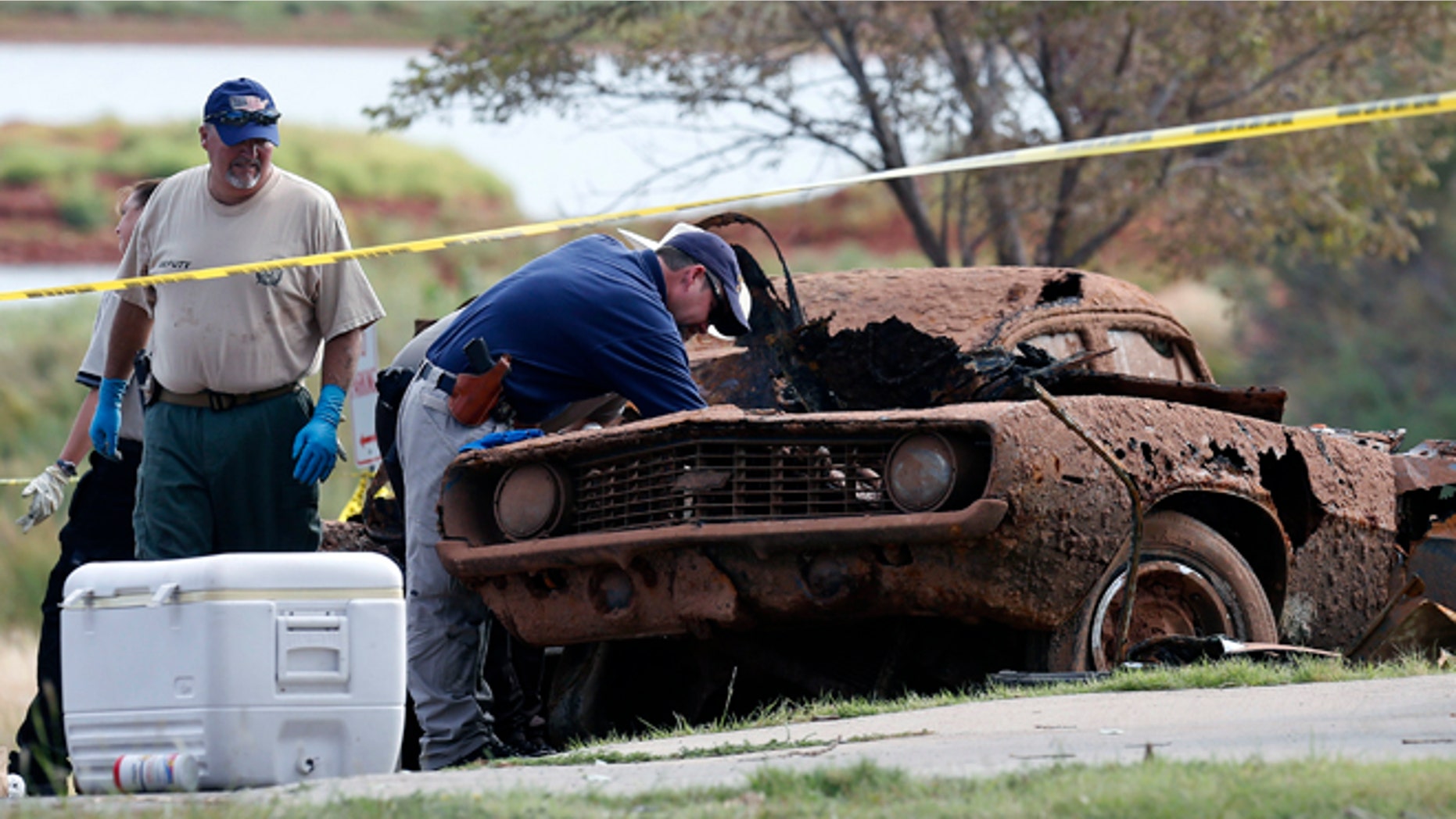 Law enforcement officials from multiple agencies examine the two cars pulled from Foss Lake, in Foss, Okla., Wednesday, Sept. 18, 2013. The Oklahoma State Medical Examinerâs Office says authorities have recovered skeletal remains of multiple bodies in the Oklahoma lake where the cars were recovered. (AP Photo/Sue Ogrocki)
