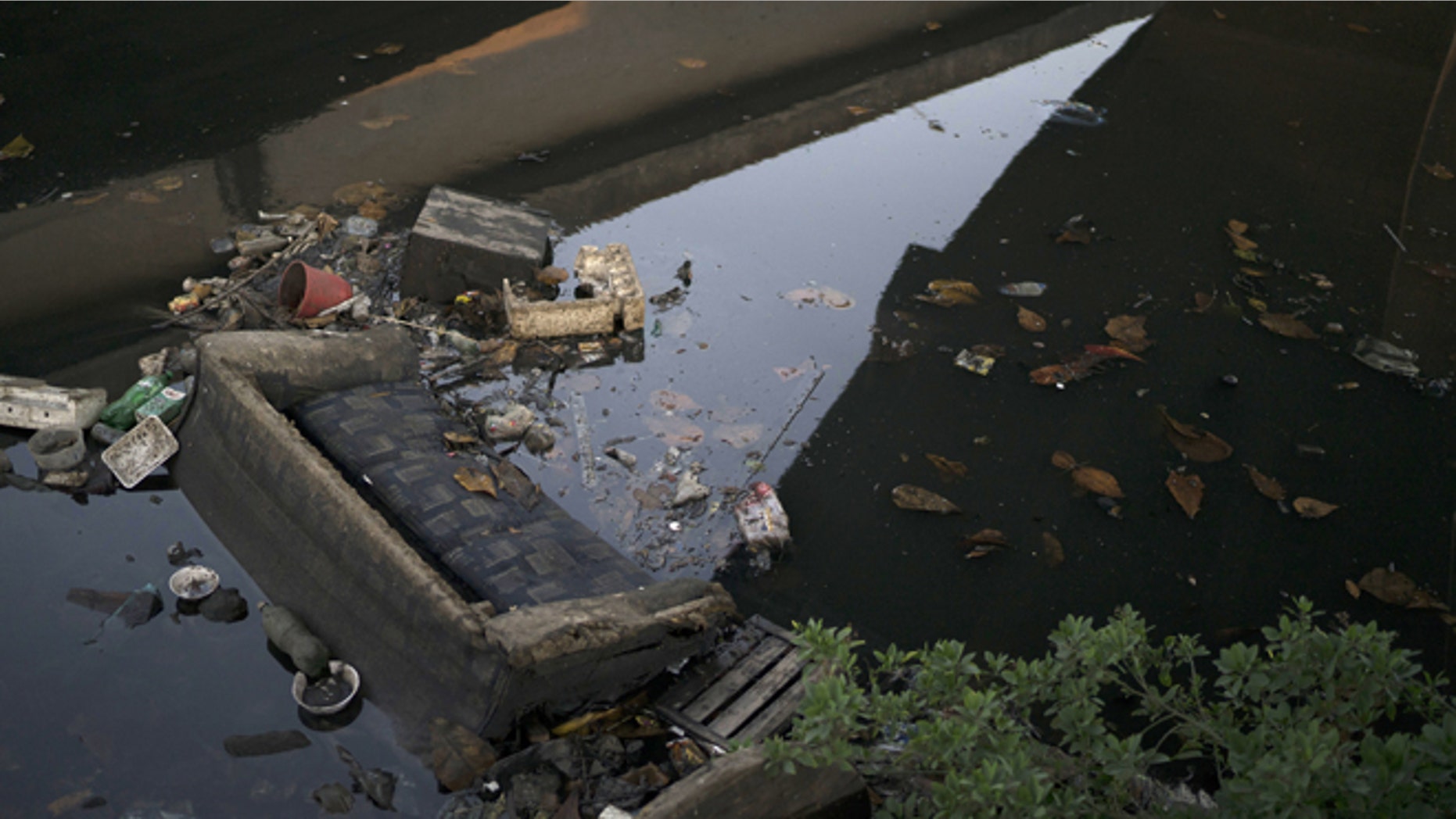 A discarded sofa lies half submerged in polluted water in a canal at the Mare slum complex in Rio de Janeiro, Brazil, Friday, July 31, 2015. In Rio, much of the waste runs through open-air ditches to fetid streams and rivers that feed the Olympic water sites and blight the city's picture postcard beaches. (AP Photo/Leo Correa)