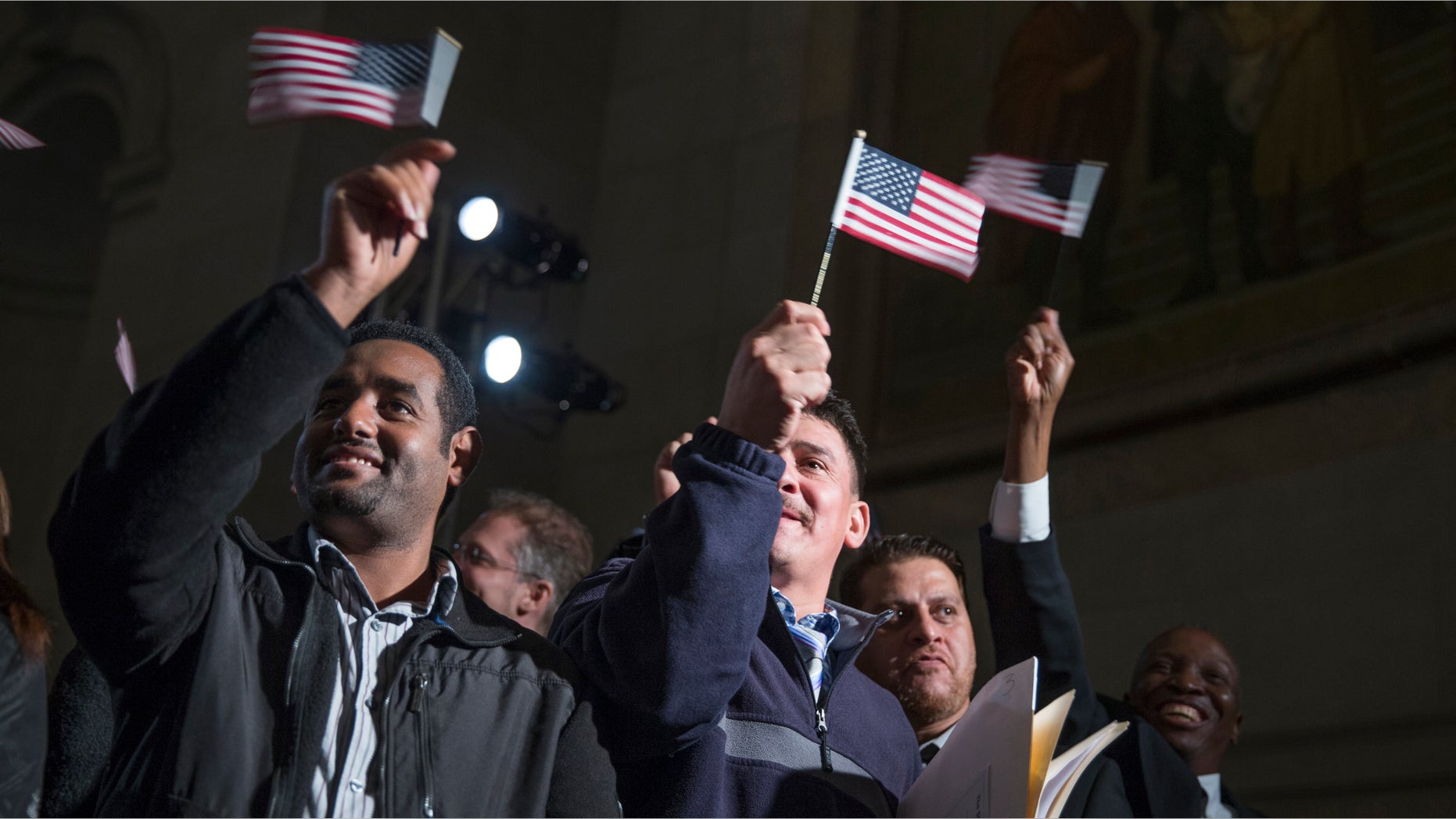 Participants in a naturalization ceremony wave flags after taking the "Oath of Allegiance" at an event attended by President Barack Obama at the National Archive in Washington, Tuesday, Dec. 15, 2015. The president spoke at the National Archives Museum, where 31 immigrants from Iraq, Ethiopia, Uganda and 23 other nations are being sworn in as U.S. citizens. (AP Photo/Evan Vucci)