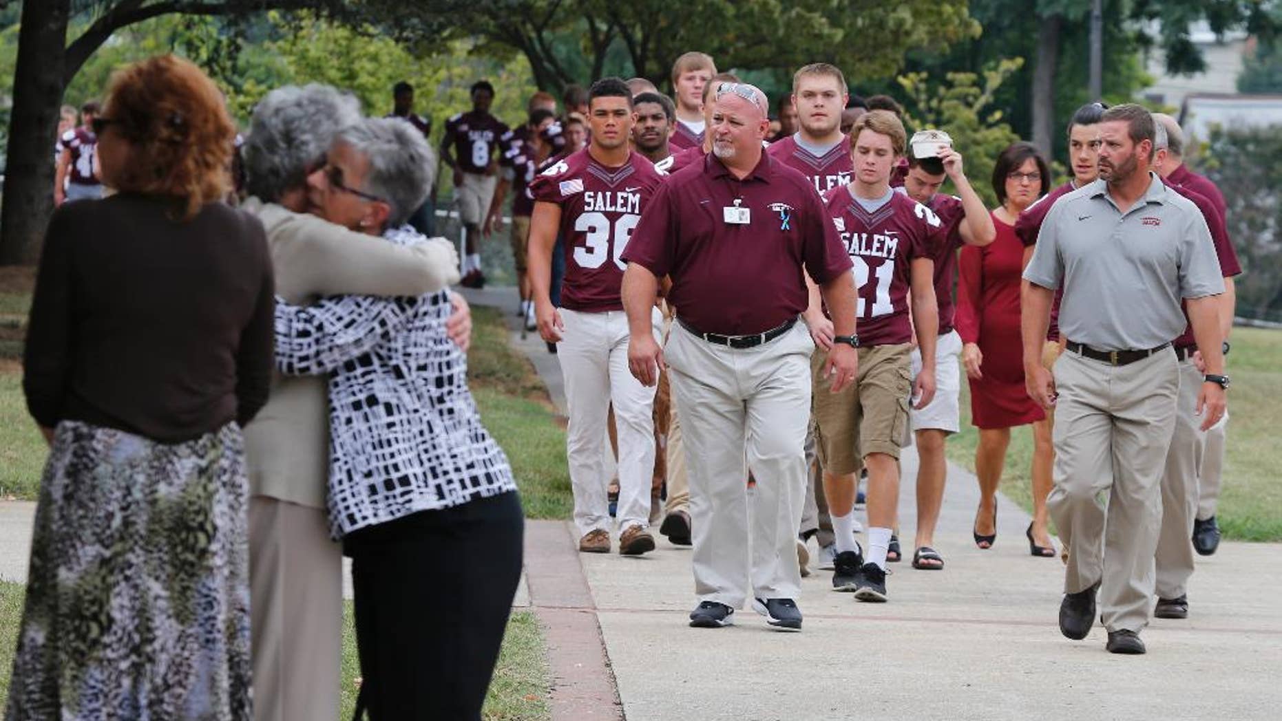 Members of the Salem High school football team arrive to remember alumnus WDBJ-TV cameraman Adam Ward, as mourners hug at Salem High School in Salem, Va., Monday, Aug. 31, 2015. Ward and reporter Alison Parker were gunned down by a former co-worker during a live shot last week. Salem High School opened its doors to the community Monday to commemorate the life of alumnus Ward. (AP Photo/Steve Helber)