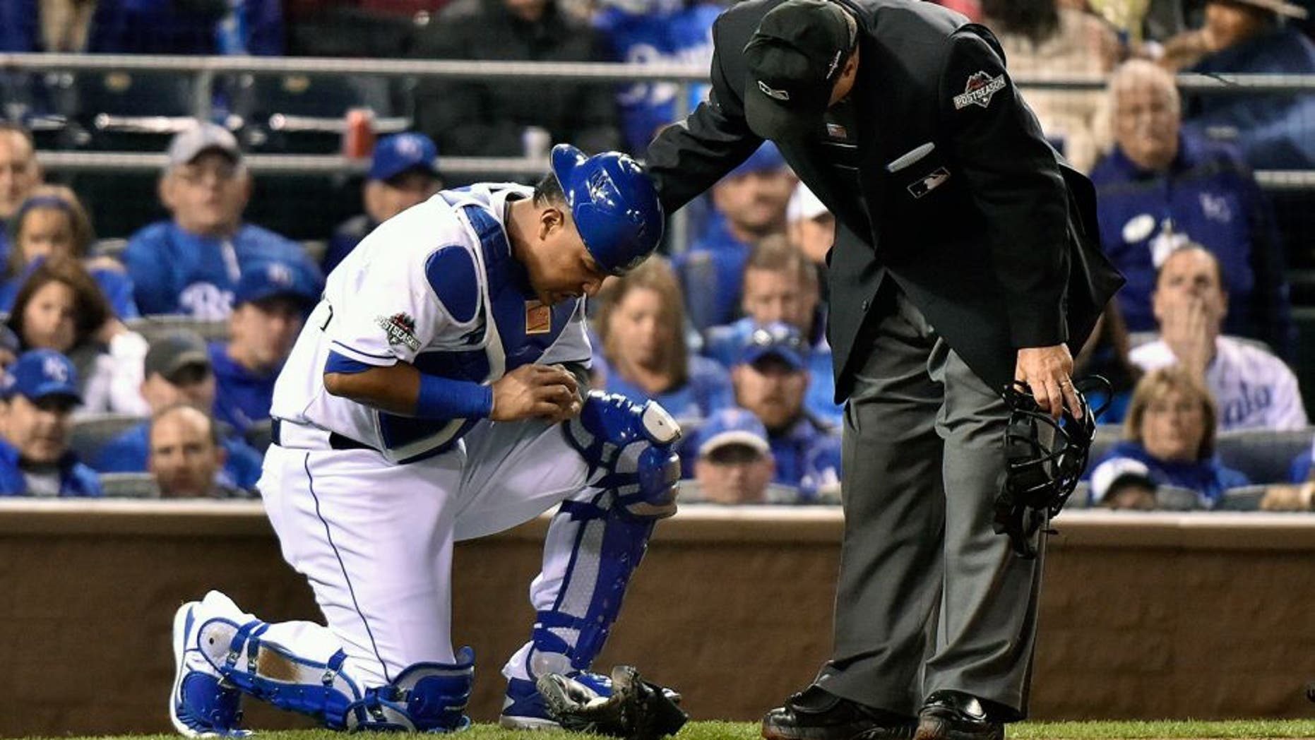 Home plate umpire Tony Randazzo, right, checks on Kansas City Royals' catcher Salvador Perez after Perez was hit on the hand by the bat of Toronto Blue Jays' Josh Donaldson during the eighth inning of Game 1 of baseball's American League Championship Series in Kansas City, Mo., Friday, Oct. 16, 2015. (Nathan Denette/The Canadian Press via AP) MANDATORY CREDIT