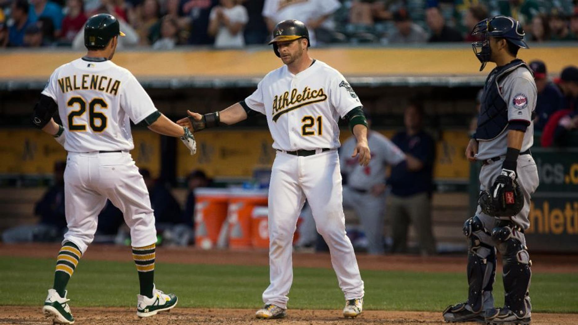 Oakland Athletics third baseman Danny Valencia is greeted by catcher Stephen Vogt after Valencia's two run home run to drive in Vogt as Minnesota Twins catcher Kurt Suzuki looks on.