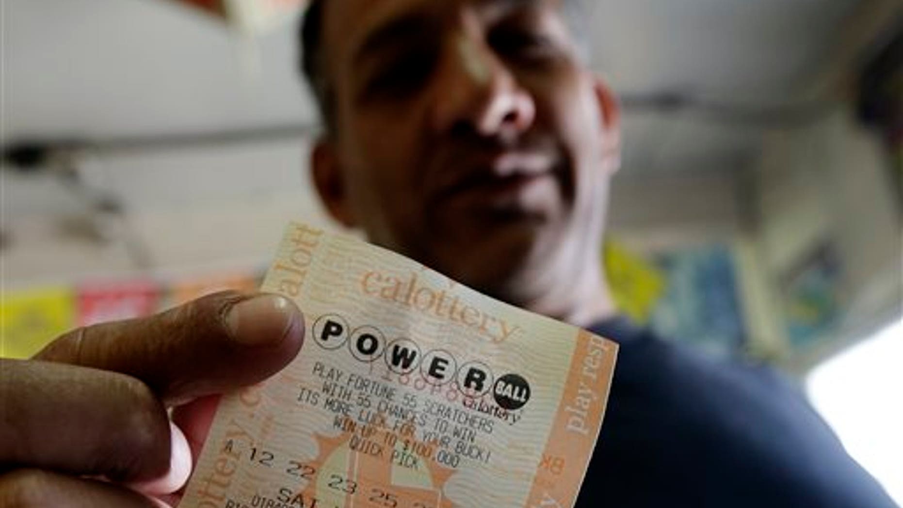 Joe Fajardo poses holding his Powerball lottery ticket after buying it at a store Saturday, May 18, 2013, in the Barrio Logan neighborhood of San Diego. With the majority of possible combinations of Powerball numbers in play, someone is almost sure to win the lottery game's highest jackpot on Saturday night, a windfall of hundreds of millions of dollars and that's after taxes. (AP Photo/Gregory Bull)