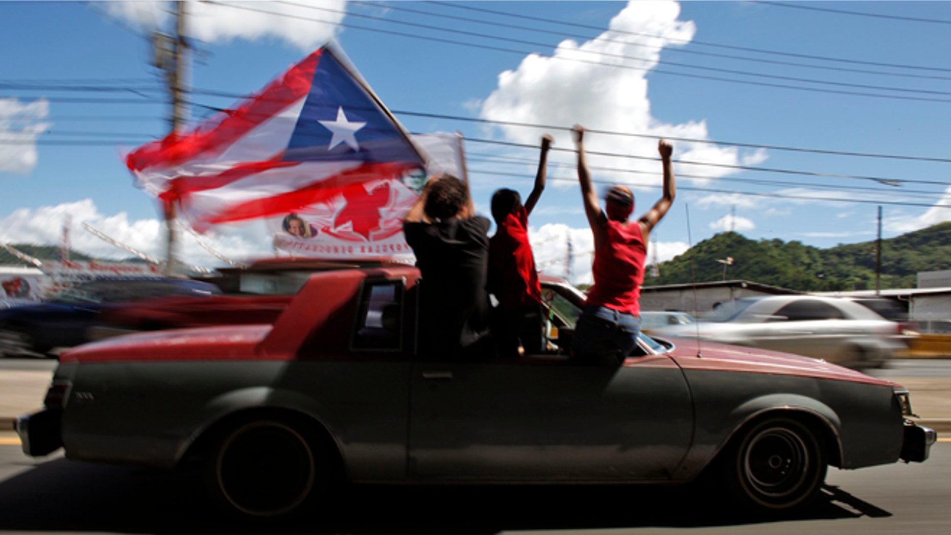 People ride atop a vehicle waving a Puerto Rican flag during elections in San Juan, Puerto Rico, Tuesday, Nov. 6, 2012. Puerto Ricans are electing a governor as the U.S. island territory does not get a vote in the U.S. presidential election. But they are also casting ballots in a referendum that asks voters if they want to change the relationship to the United States. A second question gives voters three alternatives: become the 51st U.S. state, independence, or sovereign free association, a designation that would give more autonomy. (AP Photo/Ricardo Arduengo)