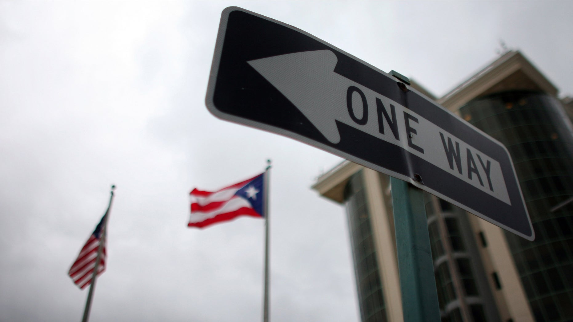 In this May 4, 2012 photo, the flags of Puerto Rico and the U.S. wave behind an English one-way traffic sign in Guaynabo, Puerto Rico, one of only a few places in Puerto Rico with street signs in English. (AP Photo/Ricardo Arduengo)