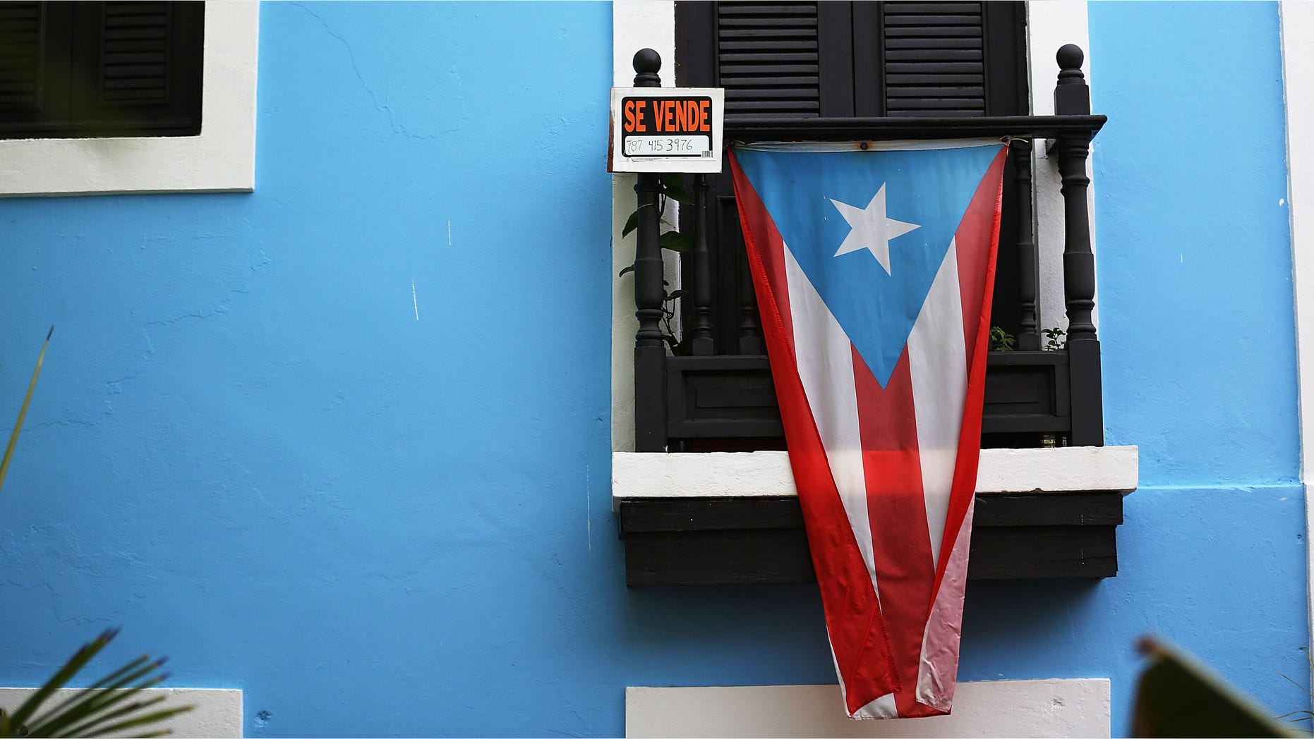 SAN JUAN, PUERTO RICO - JULY 01: A for sale sign is seen hanging from a balcony next to a Puerto Rican flag in Old San Juan as the island's residents deal with the government's $72 billion debt on July 1, 2015 in San Juan, Puerto Rico. Governor of Puerto Rico Alejandro Garc?a Padilla said in a speech recently that the people of Puerto Rico will have to make sacrifices and share the responsibilities to help pull the island out of debt. (Photo by Joe Raedle/Getty Images)