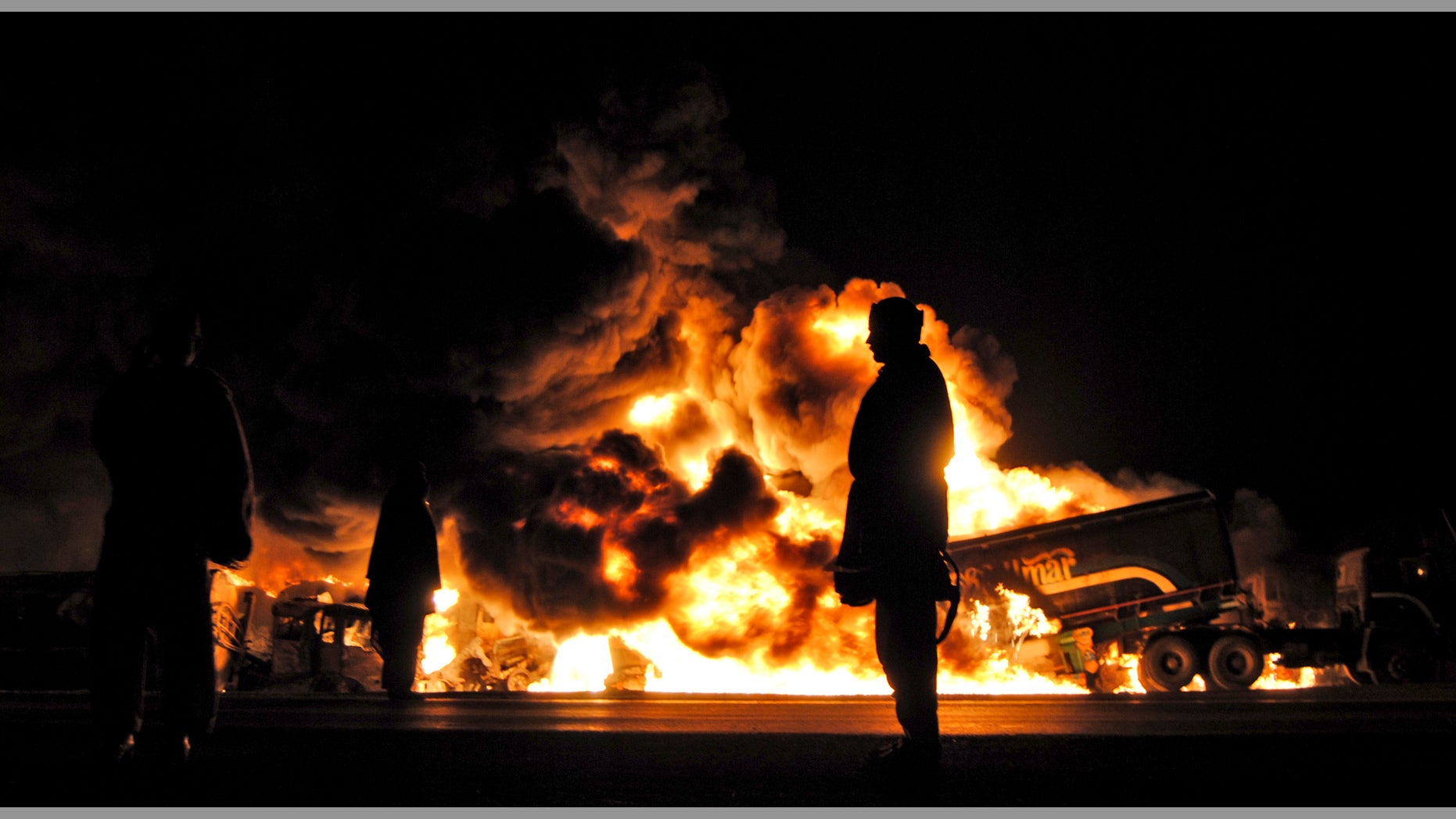 Pakistanis gather by burning oil tankers after gunmen attacked a terminal in Dera Murad Jamali southwest Pakistan, early Saturday, Jan. 15, 2011. A government official says gunmen in Pakistan's southwest have set ablaze 14 tankers carrying fuel for U.S. and NATO troops in Afghanistan. A driver also was wounded during the Saturday attack.
