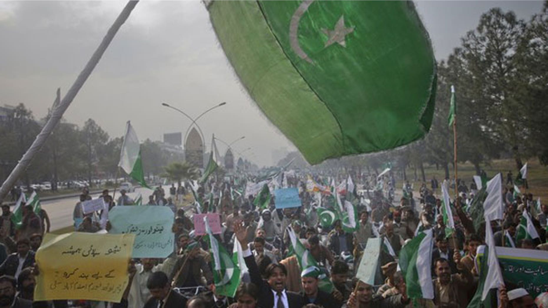 December 8, 2011: The Pakistan flag waves in the foreground as protesters hold placards during a rally in support of Pakistan army in Islamabad.