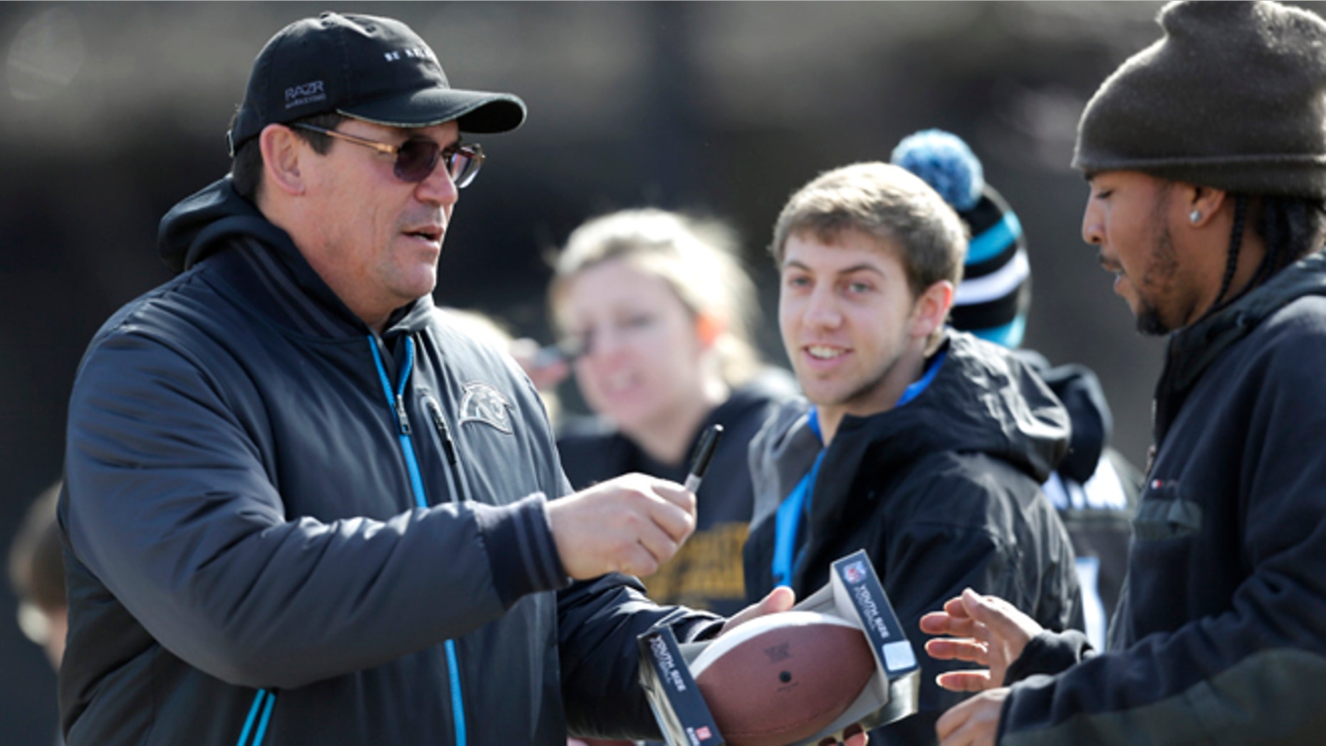 Carolina Panthers head coach Ron Rivera, left, signs autographs for fans before an NFL football practice in Charlotte, N.C., Thursday, Jan. 9, 2014. The Panthers face the San Francisco 49ers in an NFC Divisional playoff game on Sunday. (AP Photo/Chuck Burton)