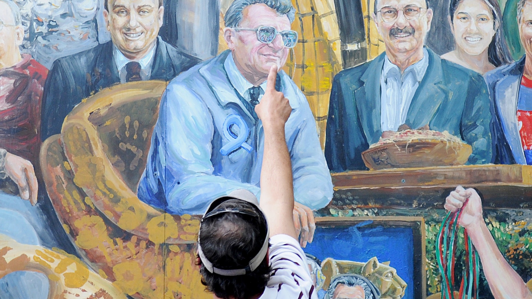 July 14, 2012: A visitor points to the spot in a mural by Michael Pilato where a halo that was above the late Penn State football coach Joe Paterno has been painted over by the artist in State College, Pa.