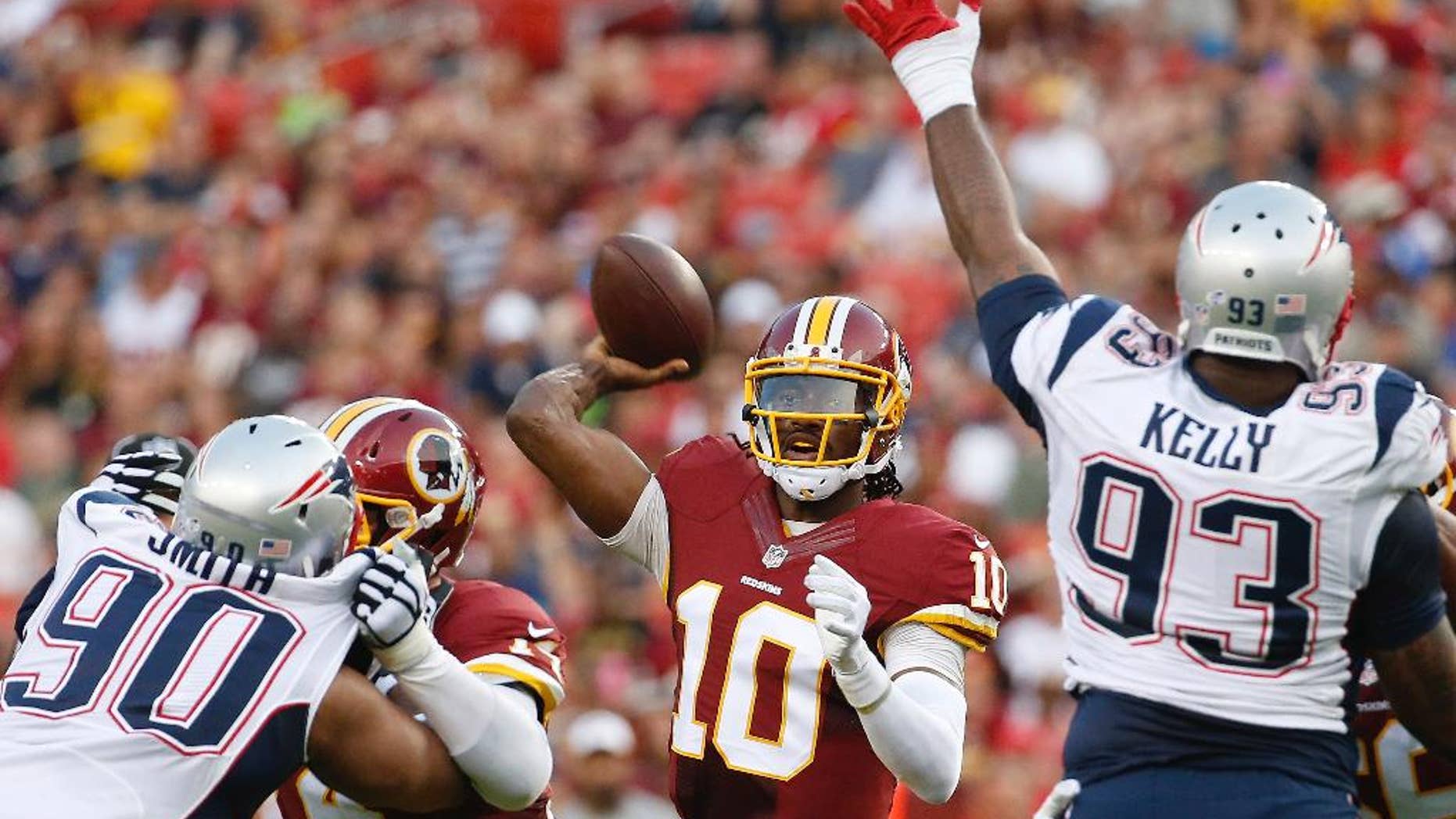 Washington Redskins quarterback Robert Griffin III passes between New England Patriots defensive end Will Smith (90) and defensive tackle Tommy Kelly (93) during the first half of an NFL football preseason game in Landover, Md., Thursday, Aug. 7, 2014. (AP Photo/Alex Brandon)