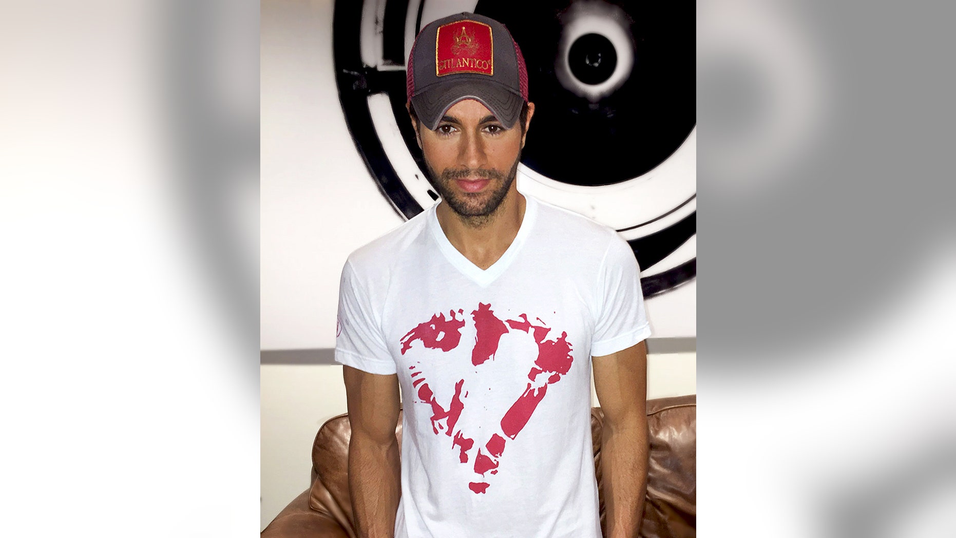 In this Sept. 30, 2015 photo provided by Enrique Iglesias, Iglesias wears his new heart T-shirt in Miami. Following an accident with a drone that led to reconstructive hand surgery, Iglesias is giving a helping hand to children dealing with emergencies. Save the Children said Monday, Oct. 26, 2015, that Iglesias is working with the organization to sell white T-shirts with a red heart at its center - mirroring how Iglesias shirt looked after he cut his fingers at a concert and wiped the blood on his shirt. (Francis Ramsden/Enrique Iglesias via AP)
