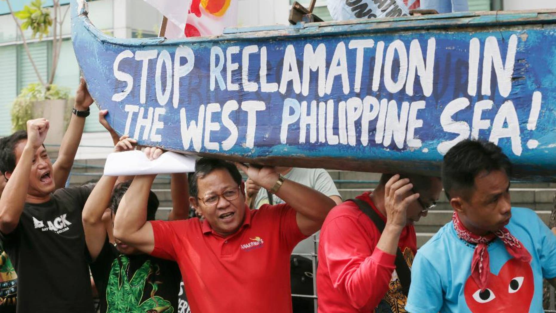 In this July 3, 2015, file photo, protesters carry a boat painted with slogans during a rally outside the Chinese Consulate at the financial district of Makati city, east of Manila, Philippines, to protest China's reclamations of disputed islands off South China Sea. China is standing pat on its decision to reject arbitration by an international tribunal that will begin formal hearings this week to resolve a long-seething feud with the Philippines over the South China Sea, Beijing's ambassador to Manila said Monday, July 6, 2015. (AP Photo/Bullit Marquez)