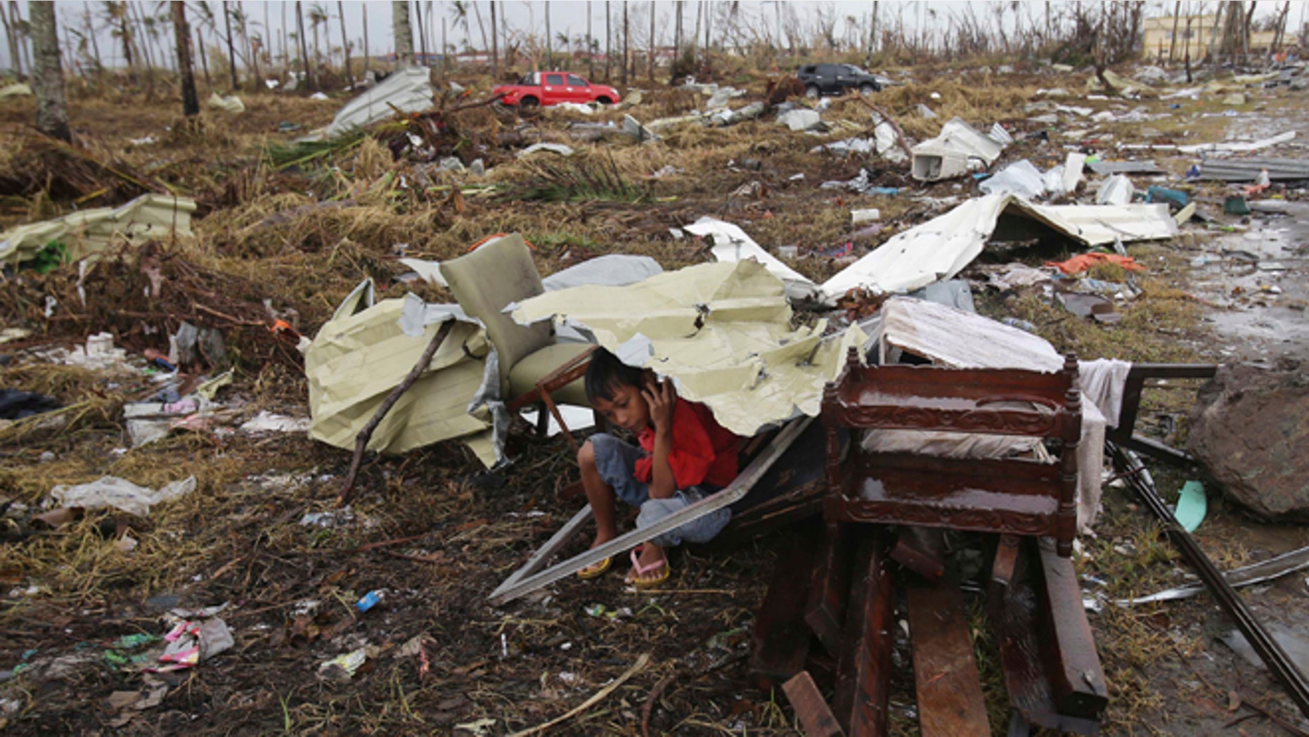 A young survivor uses the remains of some parts of a house to shield him from rain in Tacloban city, Leyte province, central Philippines on Tuesday, Nov. 12, 2013.