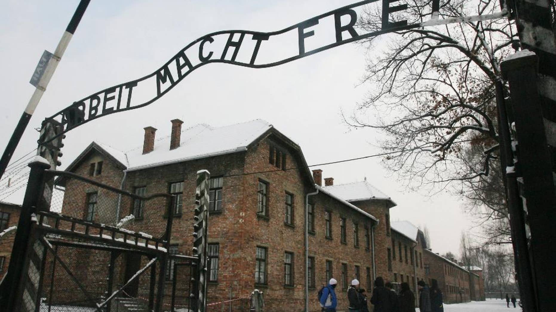 FILE - In this Dec. 18, 2009 file photo, tourists pause near the main entrance and a replica of the inscription "Arbeit Macht Frei" (Work Sets You Free) over the entrance to the former Nazi death camp Auschwitz-Birkenau, in Oswiecim, southern Poland. Authorities at the Auschwitz-Birkenau State Museum warned on Wednesday, April 22, 2015 that the number of visitors to the former German death camp is growing so high that they might have to start turning people away. (AP Photo, File) POLAND OUT