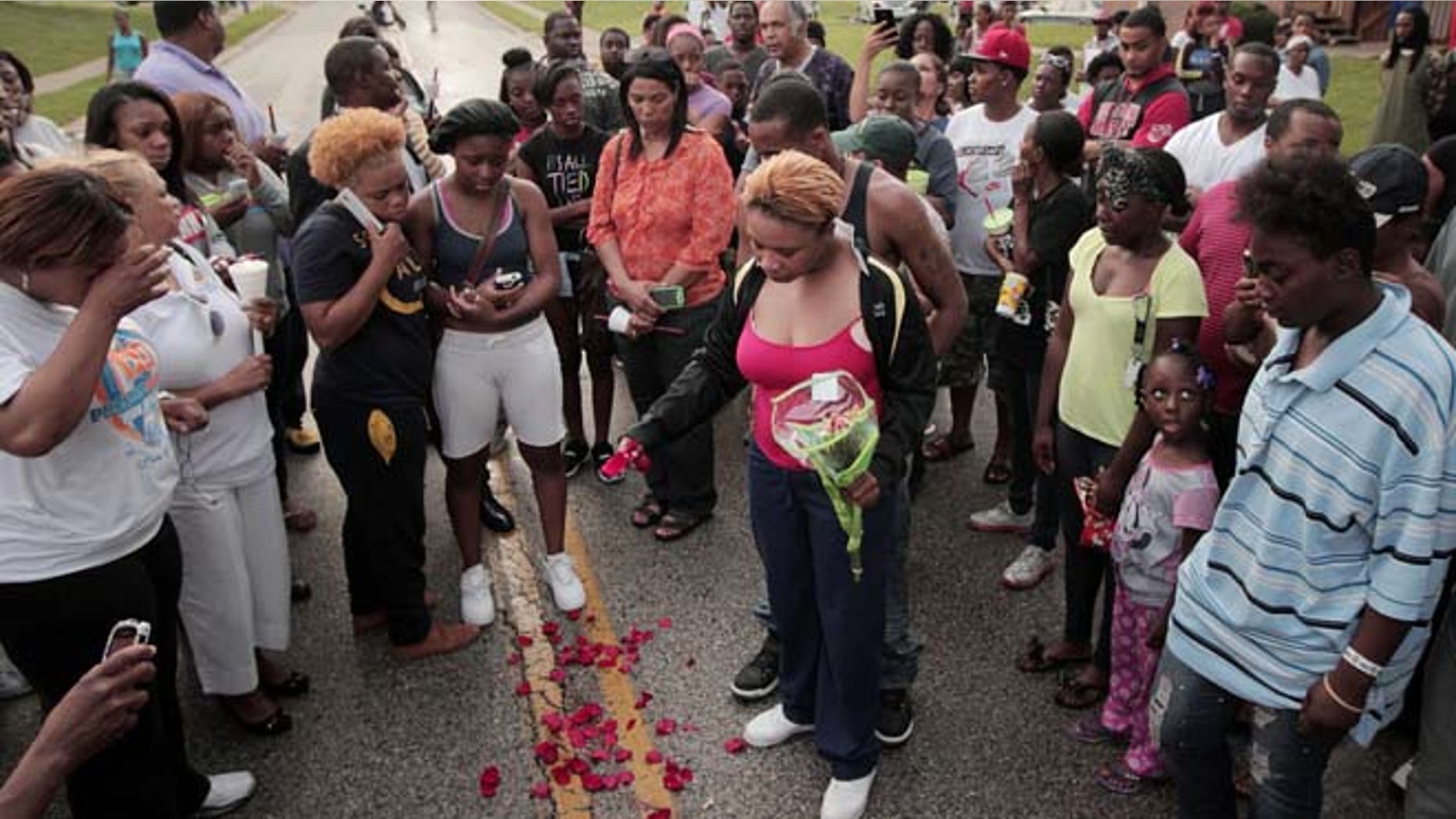 Aug. 9, 2014: Lesley McSpadden, center, drops rose petals on the blood stains from her 18-year-old son Michael Brown who was shot and killed by police in the middle of the street in Ferguson, Mo., near St. Louis. (AP/St. Louis Post-Dispatch, Huy Mach)