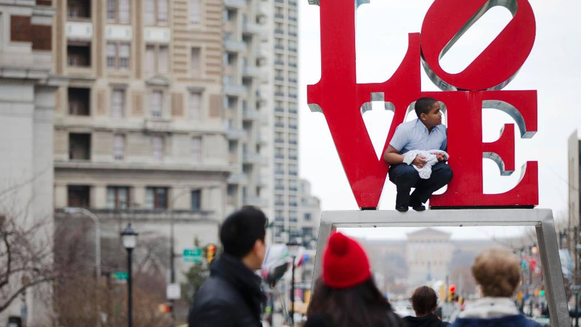 FILE - In this March 27, 2015, file photo, a young man climbs on a sculpture by Robert Indiana, at JFK Plaza, commonly known as Love Park, in Philadelphia. A bilingual version of Maine-based pop artist Indiana’s “LOVE” sculpture called the "AMOR" is going on display outside the Philadelphia Museum of Art, near where the pope’s altar is being built. (AP Photo/Matt Rourke, File)