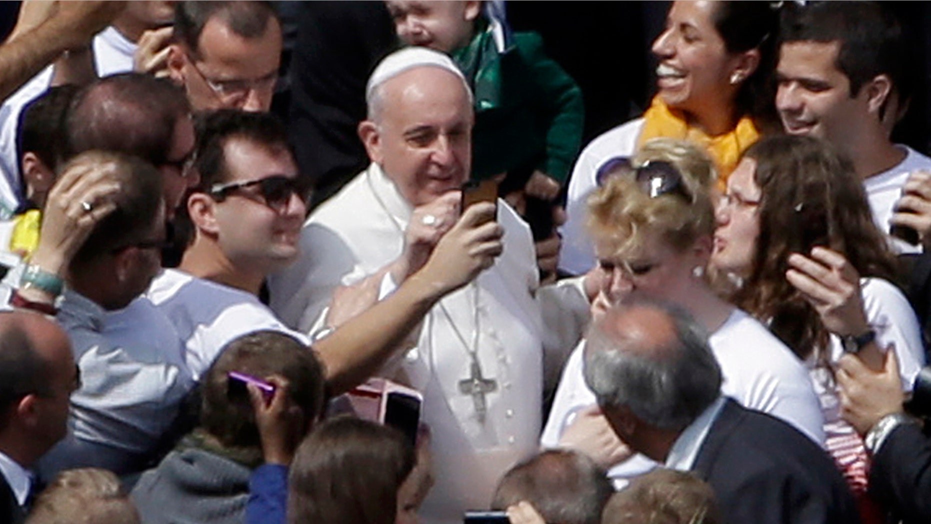 Pope Francis poses for pictures with faithful at the end of a Palm Sunday service in St. Peter's Square, at the Vatican, Sunday, April 13, 2014. Pope Francis, marking Palm Sunday in a packed St. Peter's Square, ignored his prepared homily and spoke entirely off-the-cuff in a remarkable departure from practice. Later, he hopped off his popemobile to pose for "selfies" with young people in the crowd. In his homily, Francis called on people, himself included, to look into their own hearts to see how they are living their lives. (AP Photo/Gregorio Borgia)