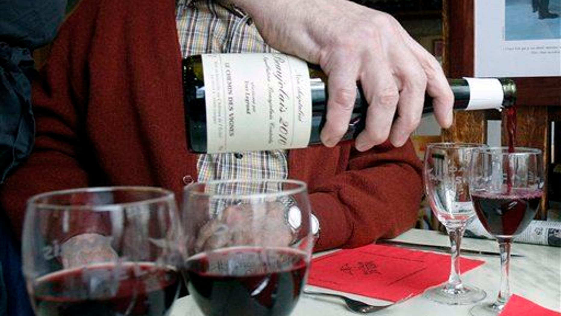 Restaurant owner Jacques Melac pours Beaujolais Nouveau wine in his customers' glasses in Paris, Nov. 18, 2010.