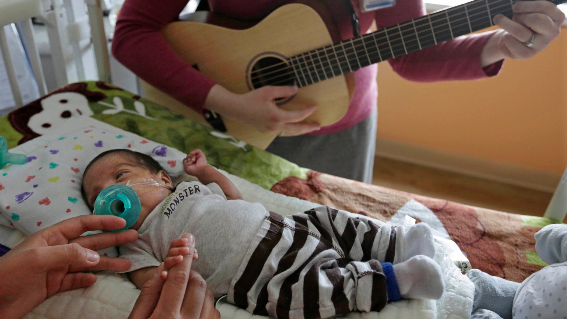 Music therapist Elizabeth Klinger, right, quietly plays guitar and sings for Augustin as he grips the hand of his mother, Lucy Morales, in the newborn intensive care unit at Ann & Robert H. Lurie Children's Hospital in Chicago.
