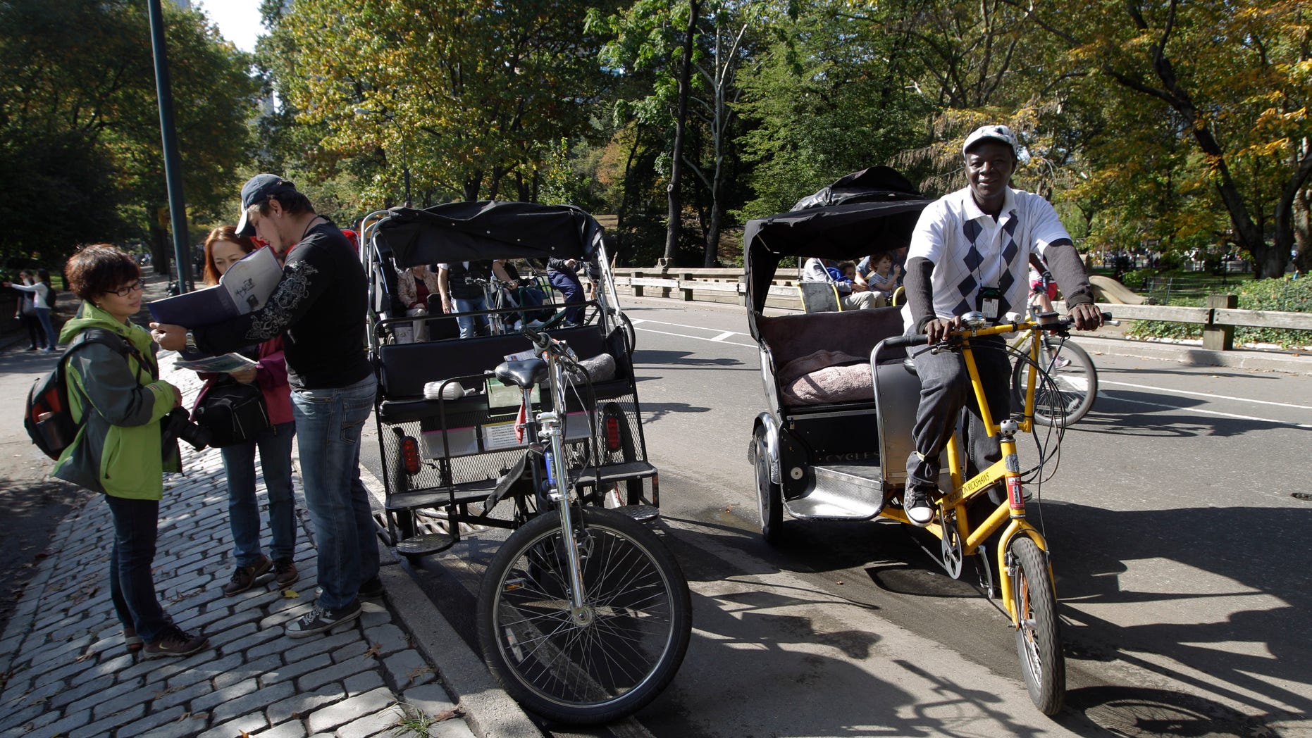 Oct. 20 2012: A pedicab driver, left, shows potential customers a map with of the tour of New York's Central Park while another looks for customers.